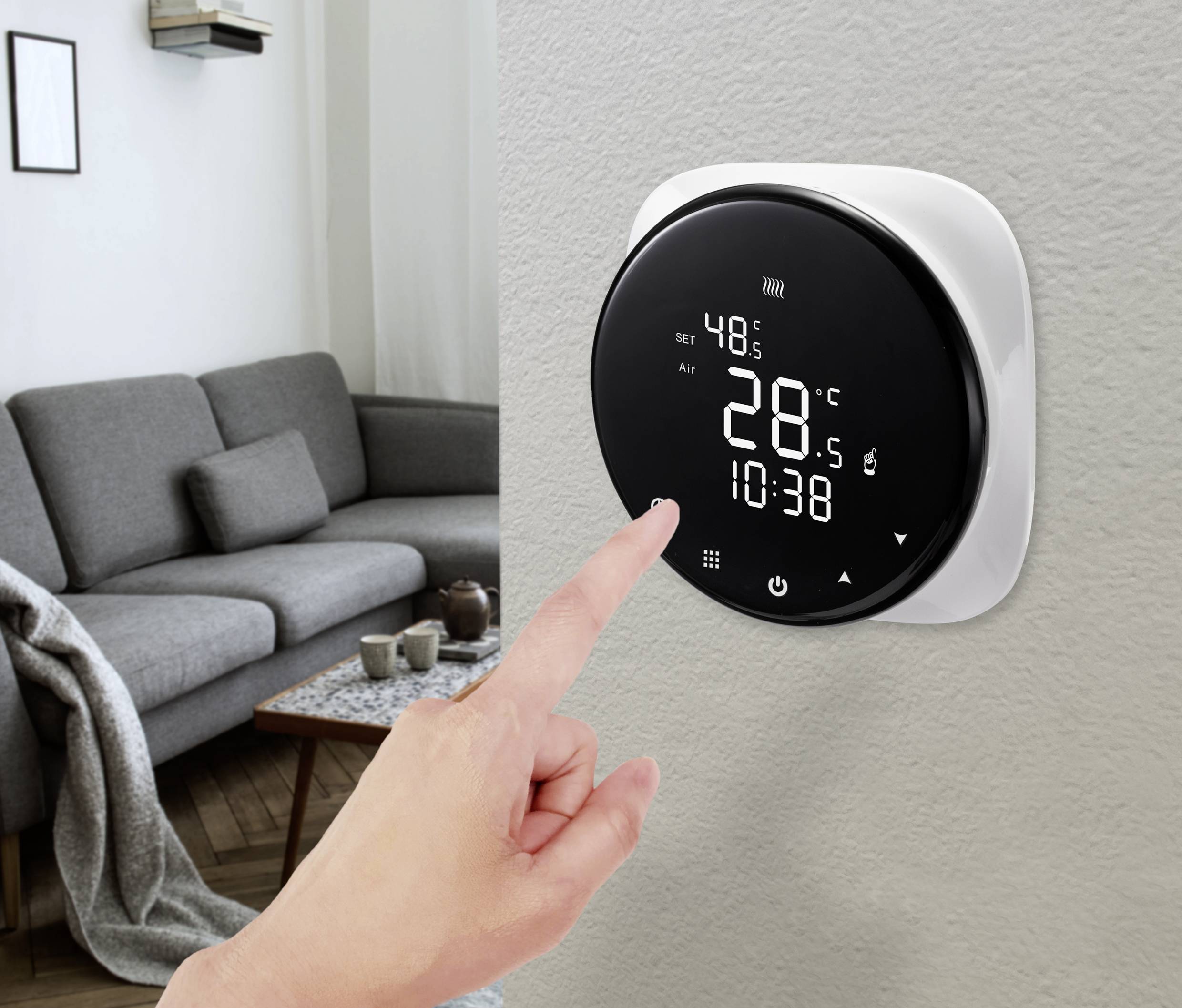 Ein Finger berührt einen digitalen Thermostat an der Wand in einem Wohnzimmer. Der Bildschirm zeigt 28°C und die Uhrzeit 10:38 an.
