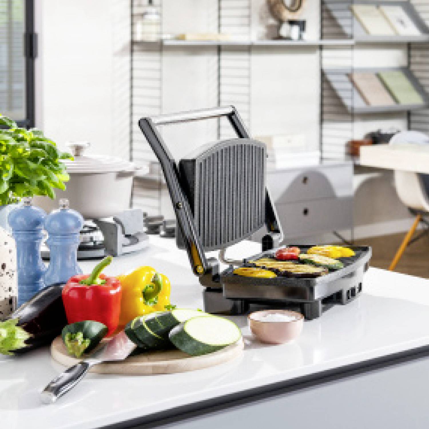 Auf einem Küchentresen sieht man einen geöffneten Grill mit gegrilltem Gemüse. Davor liegen weiteres Gemüse und Küchenutensilien.