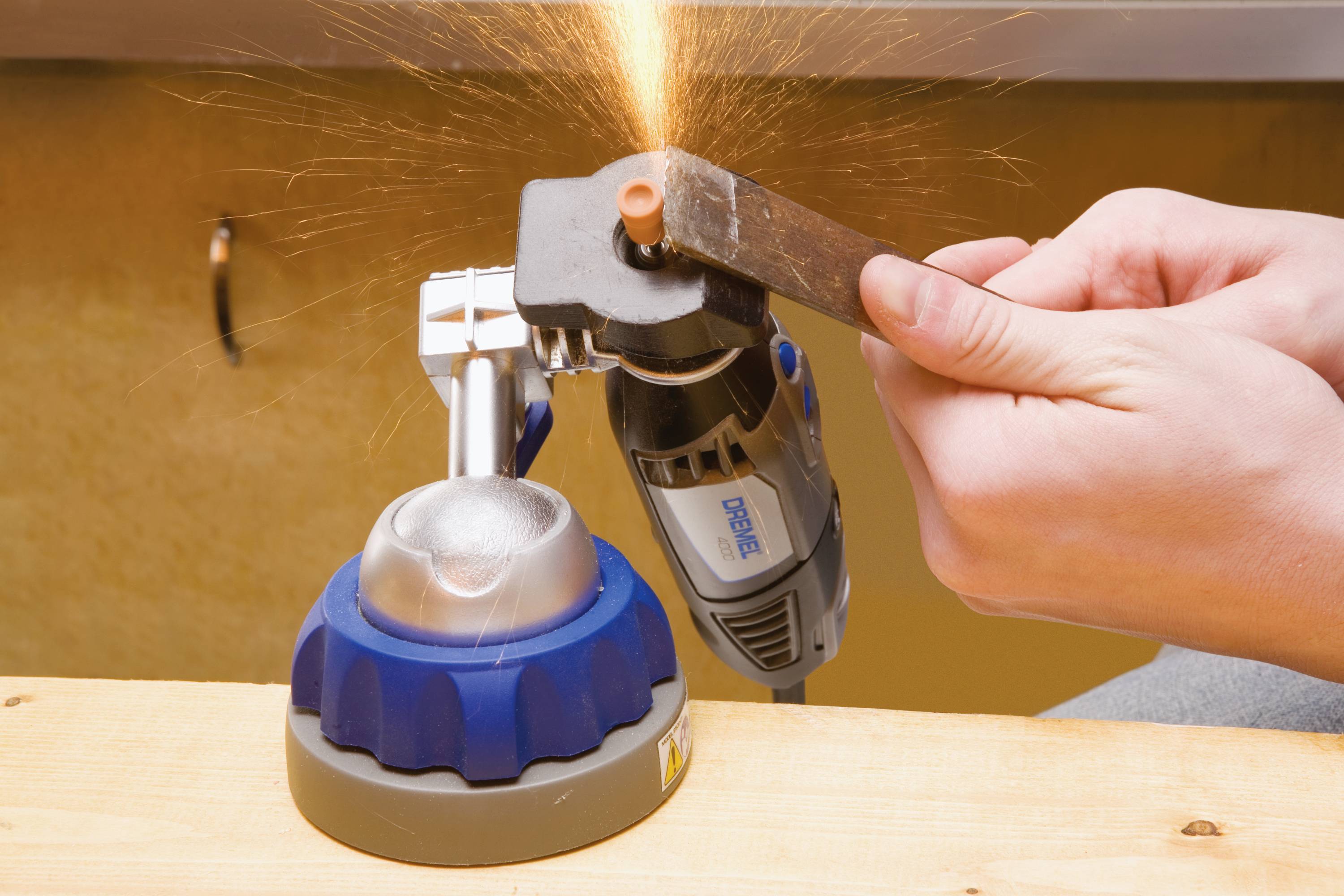 Eine Person schleift Metall mit einem Dremel-Werkzeug, wobei Funken sprühen. Das Werkzeug ist in eine Halterung eingespannt.