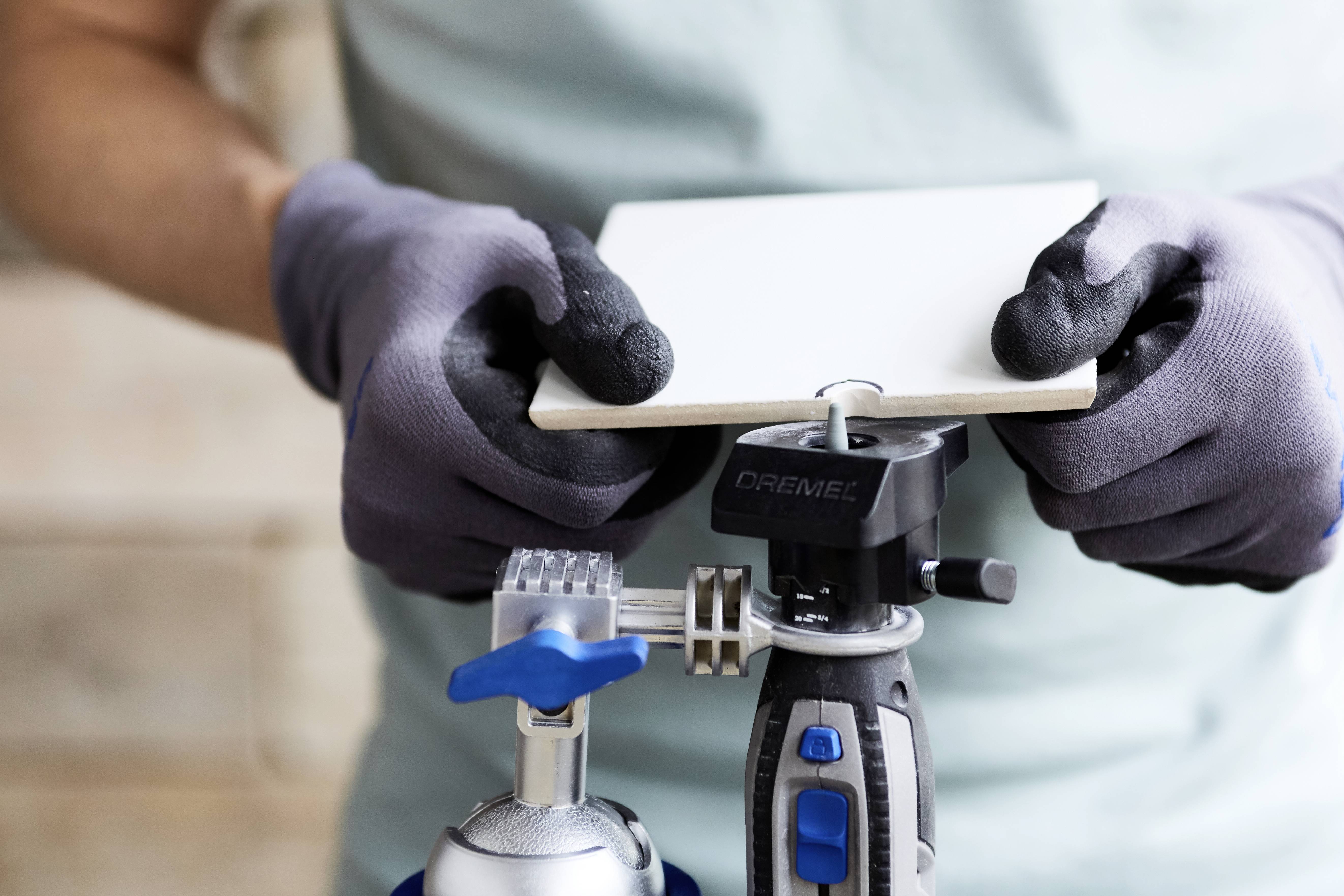 Eine Person trägt Arbeitshandschuhe und hält eine weiße Fliese über einem Werkzeug, vermutlich im Rahmen eines Heimwerkerprojekts.
