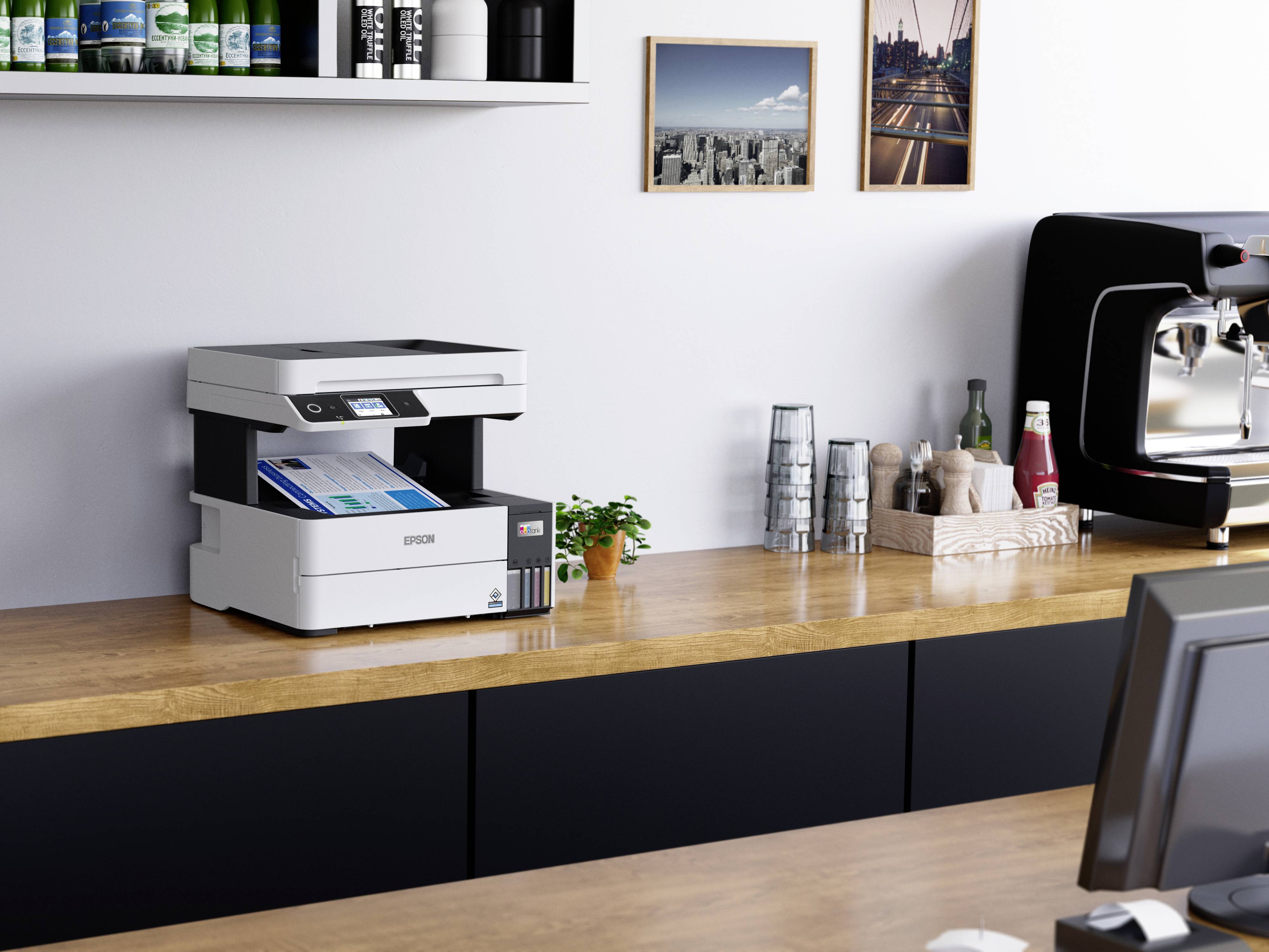 Ein moderner Drucker steht auf einem Holztisch in einem Büro oder einer Küche. Im Hintergrund sind Regale mit Tassen und Dekorationen.