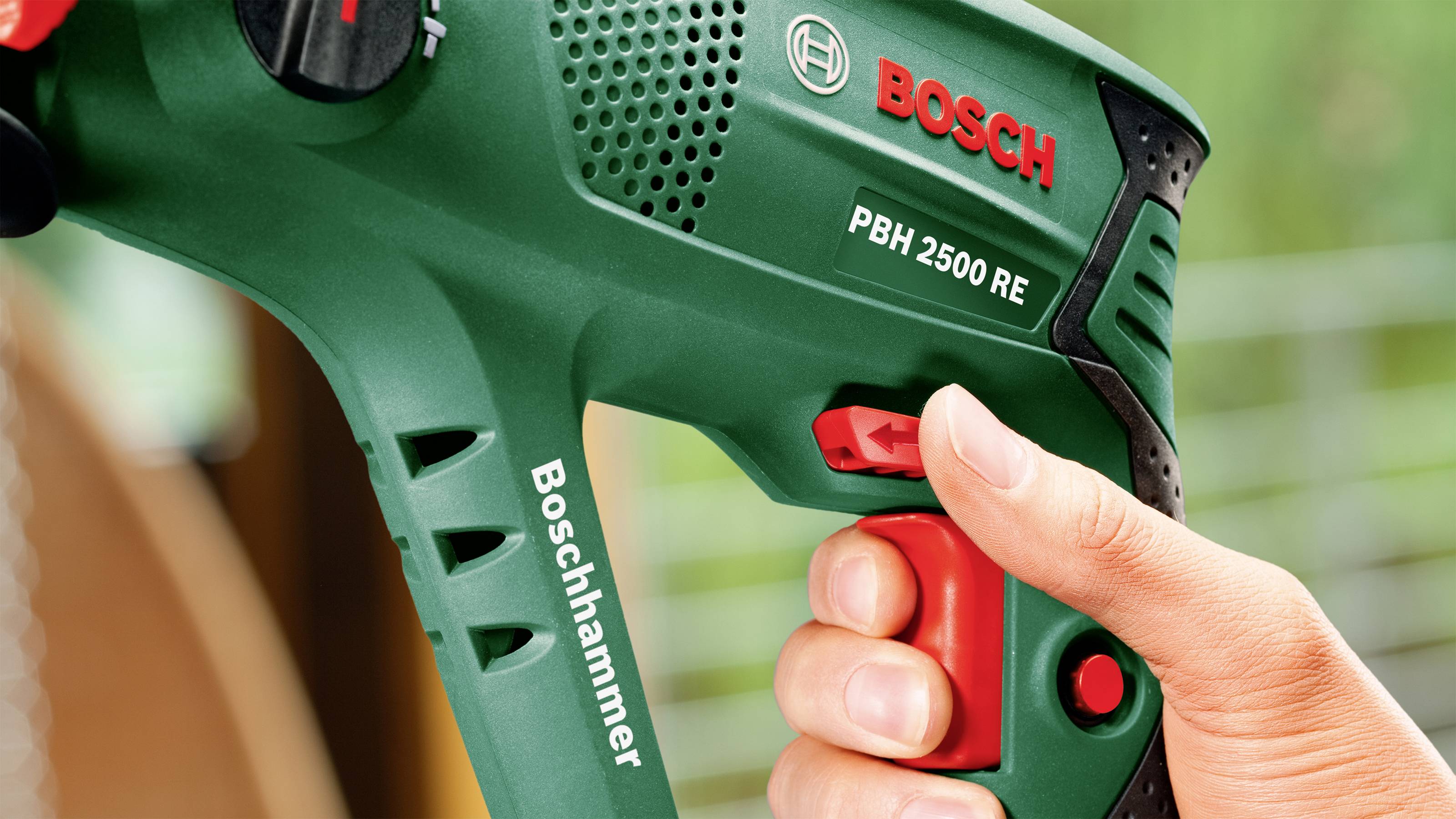 Eine Hand hält einen grünen Bosch-Bohrhammer 'PBH 2500 RE', der für leistungsstarkes Bohren und Meißeln verwendet wird.