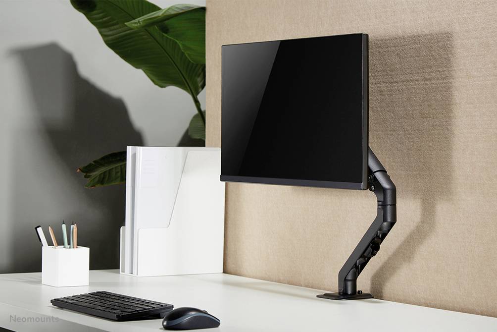 Ein minimalistischer Schreibtisch mit einem Monitor, der an einem verstellbaren Arm befestigt ist. Links befinden sich Stifte und Dokumente.