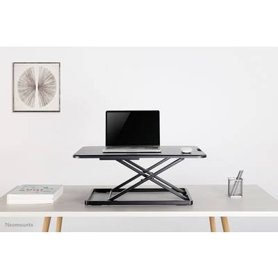Ein höhenverstellbarer Schreibtischaufsatz mit einem Laptop und einer Maus darauf. Im Hintergrund ein Kunstwerk und ein Stifthalter.