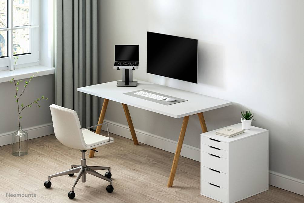 Helles, modernes Büro mit einem weißen Schreibtisch, Computerbildschirmen, einem weißen Bürostuhl auf Rollen und einer kleinen Pflanze.