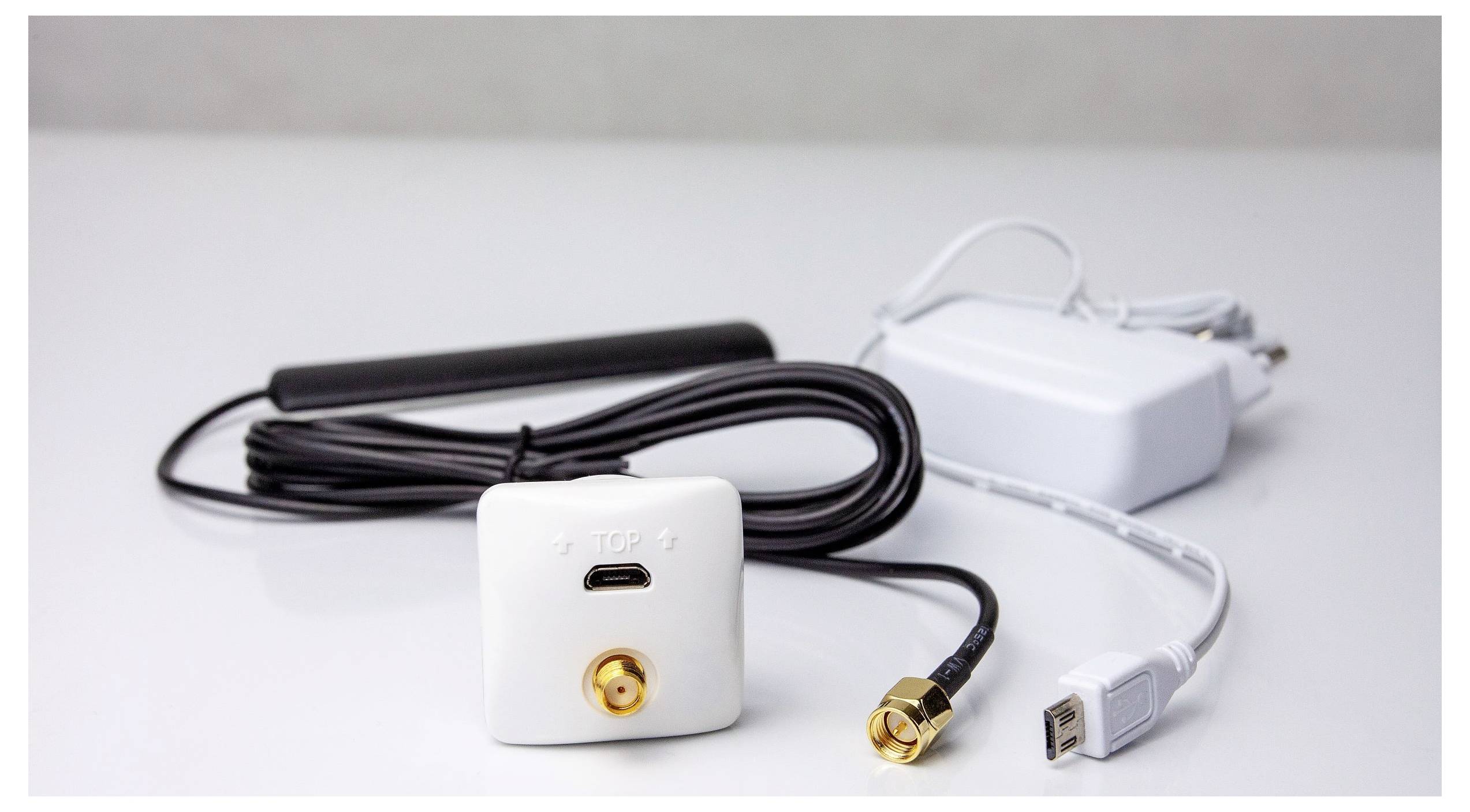 Ein weißes Netzwerkgerät mit Kabeln und einer Antenne, das einen goldenen Anschluss und einen USB-Port aufweist, auf einer weißen Oberfläche platziert.