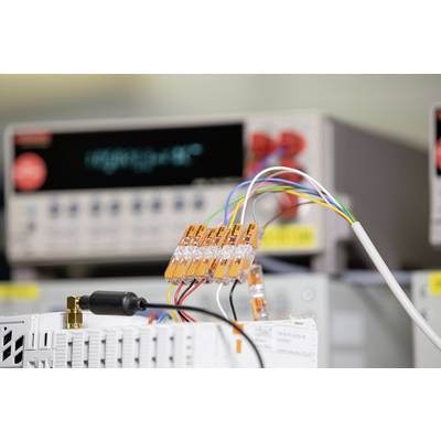 Ein Labor mit elektrischen Messgeräten im Hintergrund. Im Vordergrund sind Kabel mit orangefarbenen Klemmen verbunden.
