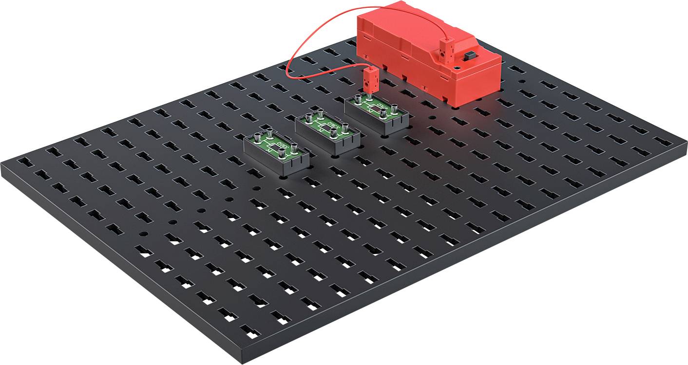 Schwarze perforierte Platte mit zwei kleinen grünen Schaltkreisen und rotem Batteriegehäuse, das mit einem Kabel verbunden ist.