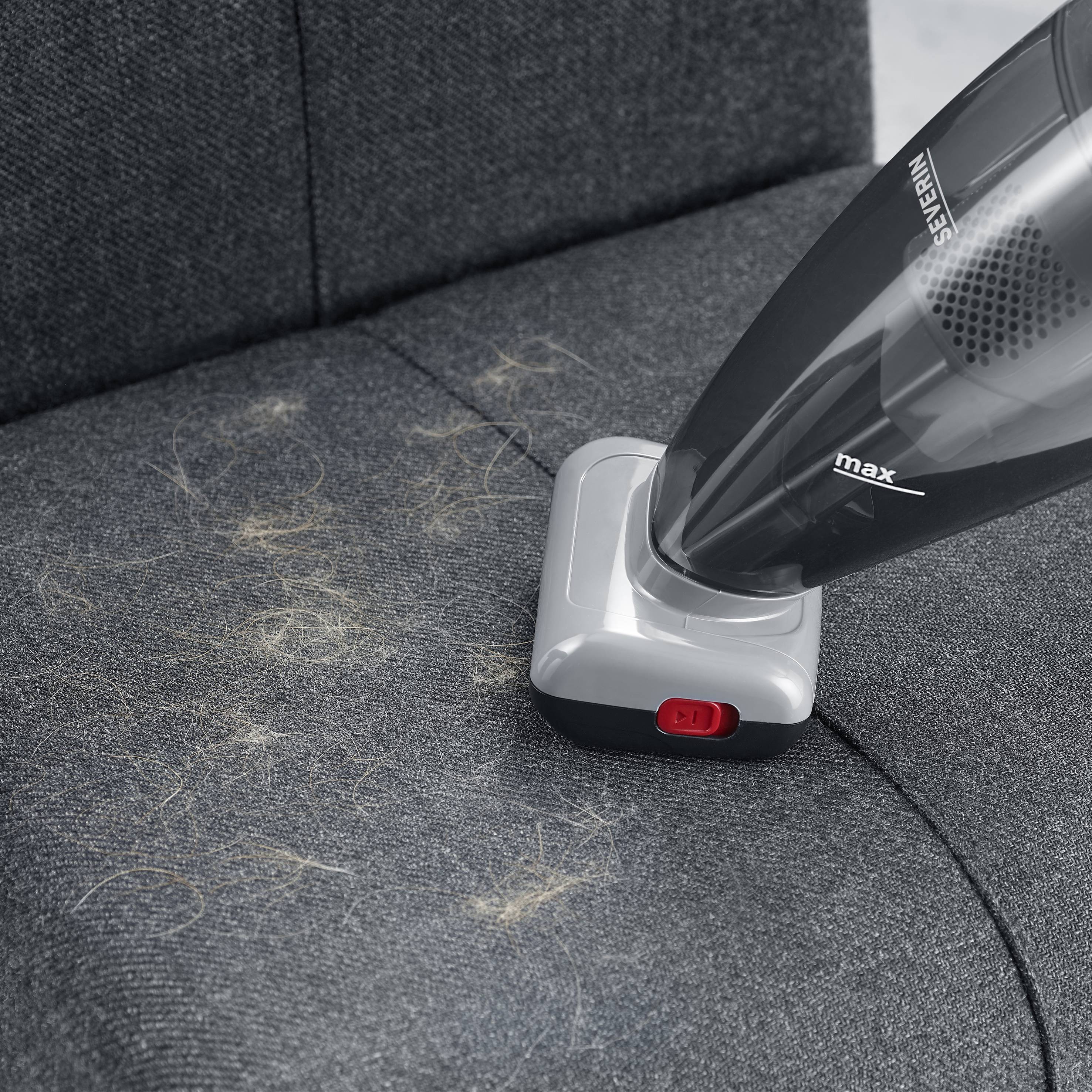 Ein Handstaubsauger entfernt Tierhaare von einem grauen Stoffsofa.