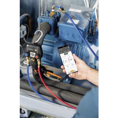 Eine Hand hält ein Smartphone mit einer App zur Temperatur- und Drucküberwachung vor einer industriellen Maschine mit blauen Schläuchen.