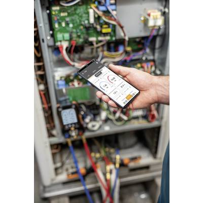 Eine Person hält ein Smartphone mit einer App zur Überwachung von Geräten vor einem geöffneten elektrischen Schaltschrank.