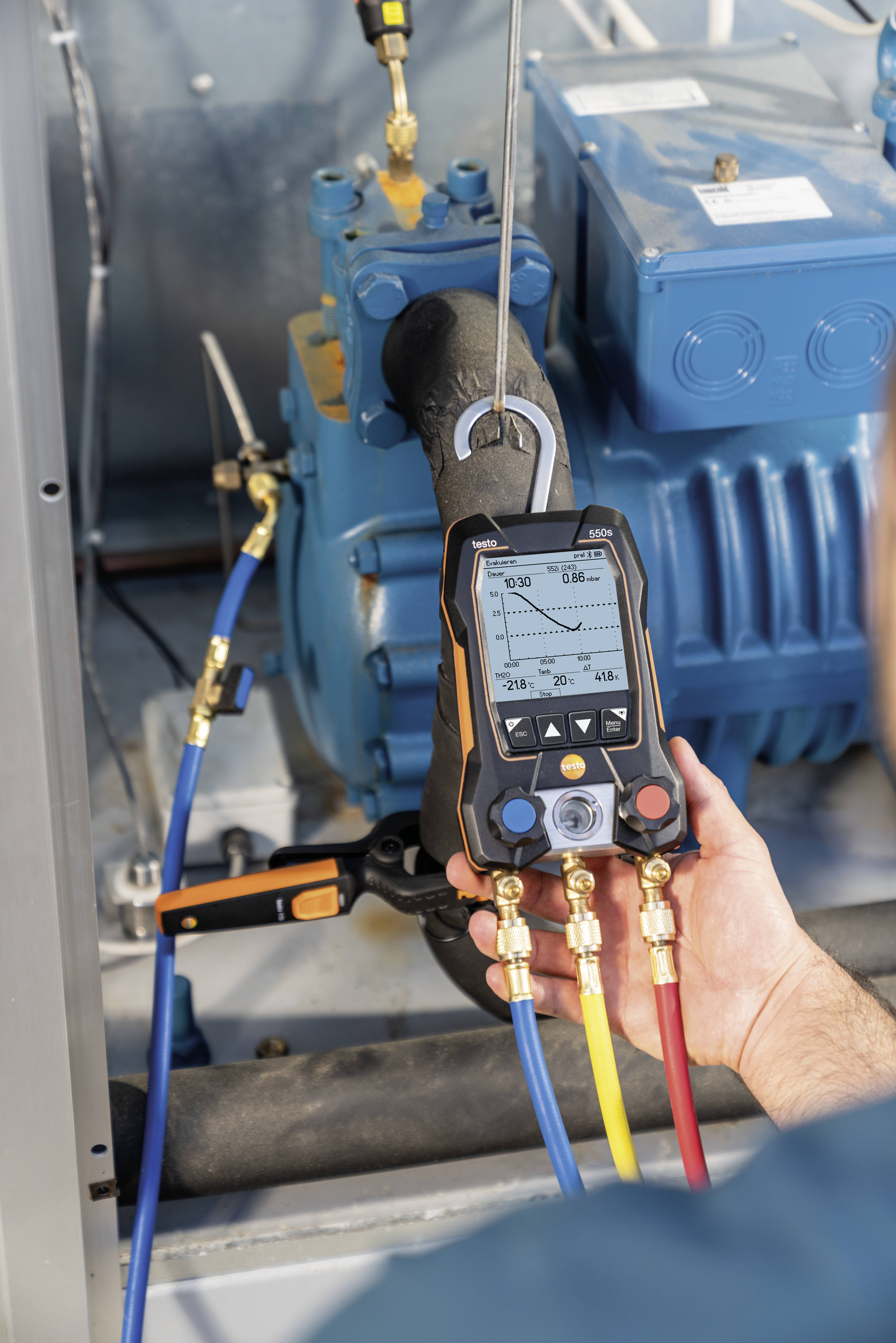 Eine Person misst mit einem digitalen Manometer den Druck in einem blauen technischen Gerät. Das Display zeigt verschiedene Druckwerte.