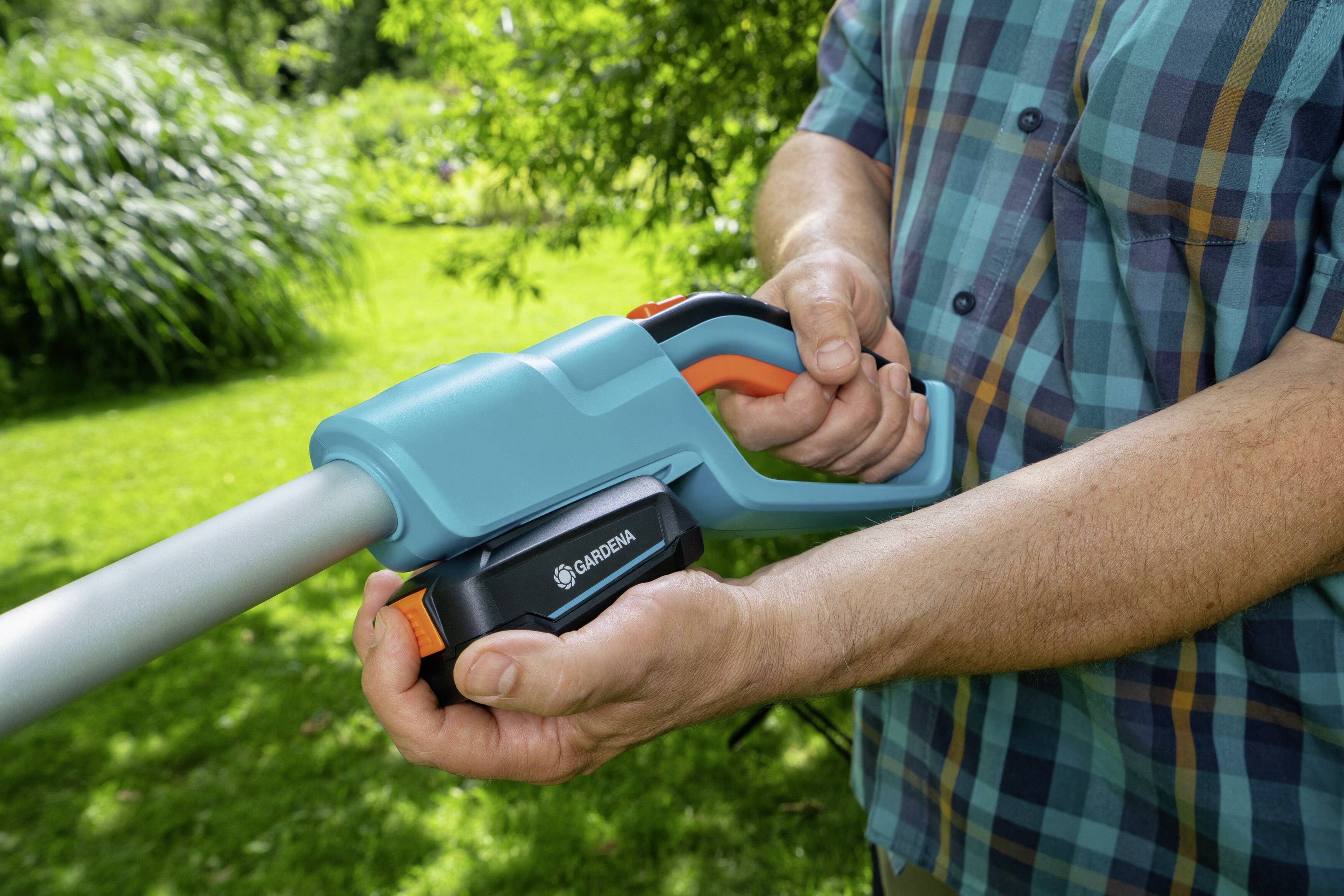 Eine Person hält eine Gardena-Heckenschere im Garten. Die Hand liegt am Griff, bereit zum Einsatz. Im Hintergrund ist grünes Gras sichtbar.