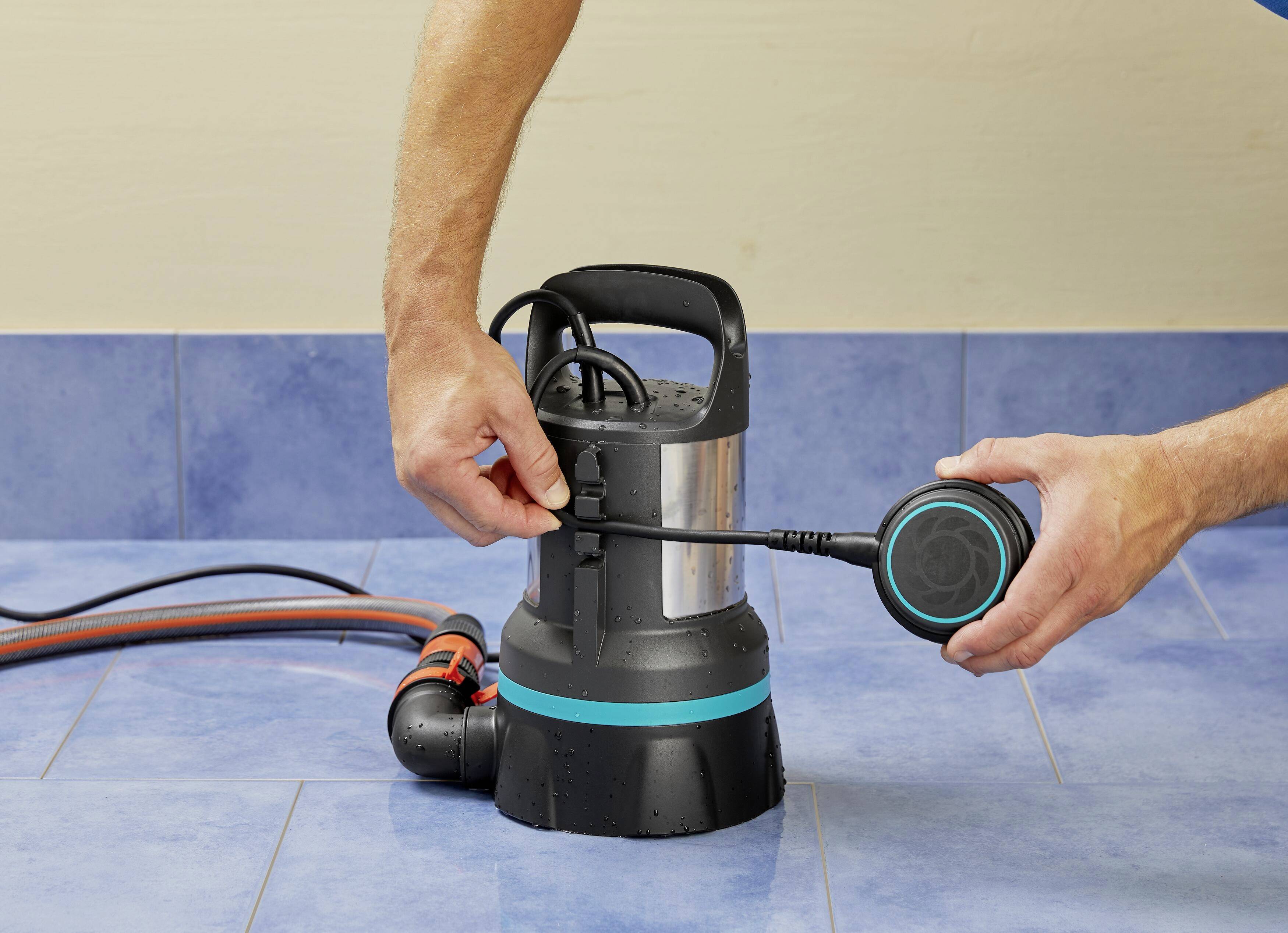 'Eine Person montiert eine elektrische Wasserpumpe auf blauem Boden, sie hält einen Teil der Pumpe in der rechten Hand.'