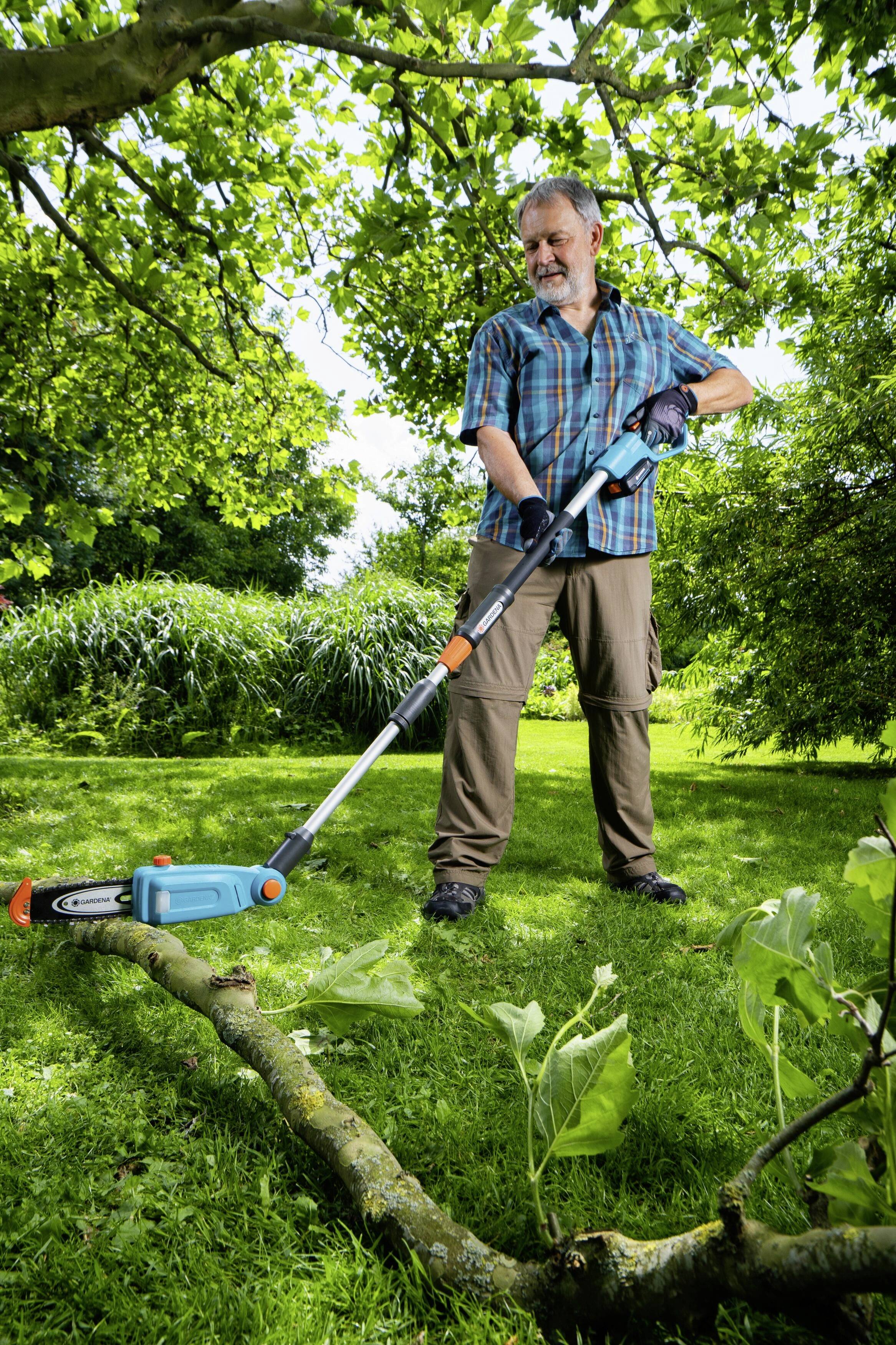 Ein Mann im Garten schneidet einen abgesägten Ast mit einem Elektro-Trimmer. Umgeben von grünen Bäumen und Gras.