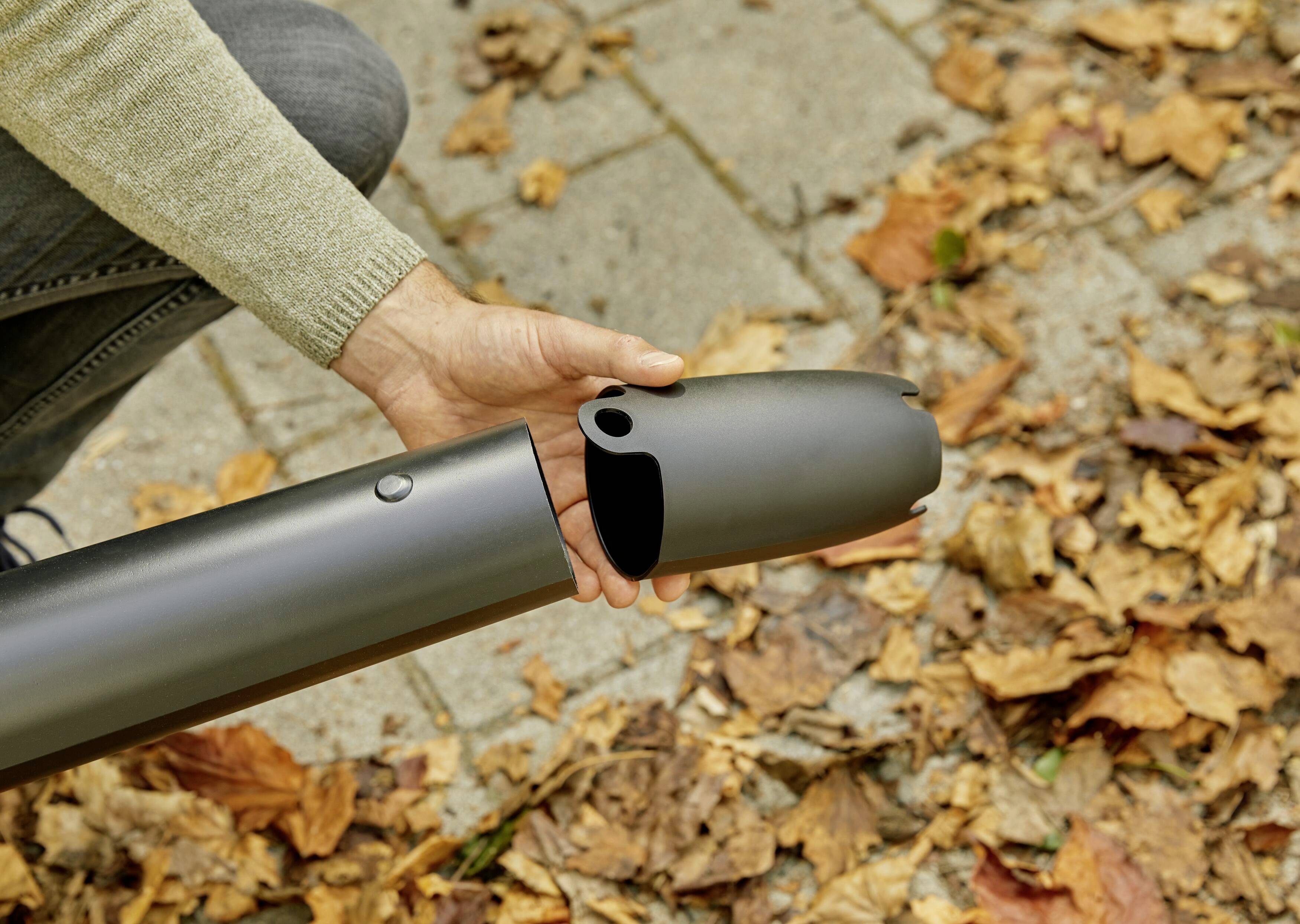 Eine Person hält ein abnehmbares Teil eines zylindrischen Objekts über Herbstblätter auf einem Gehweg.