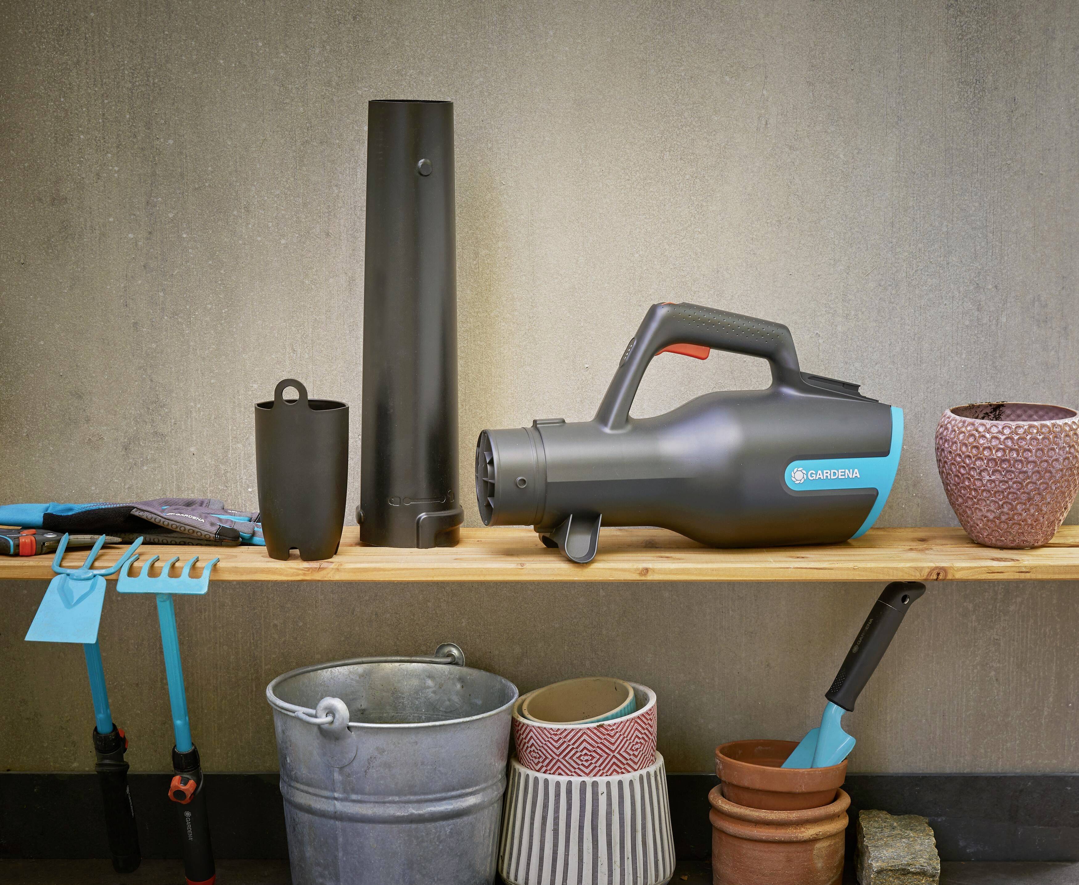 Gartengeräte und Blasgerät auf einem Holzregal. Plastikeimer und Töpfe stehen darunter. Essenziell für Gartenarbeit.
