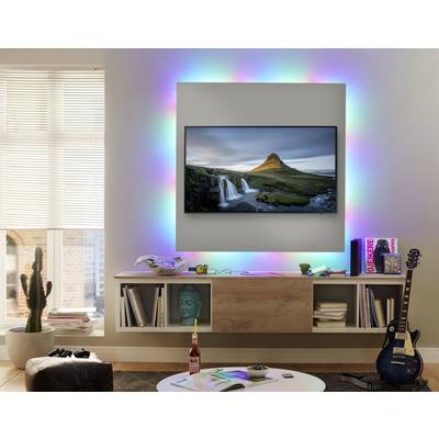 Flachbildschirm an der Wand mit einem Landschaftsbild, umgeben von bunten LED-Leuchten. Darunter stehen Bücher, eine Gitarre und Dekorationen.