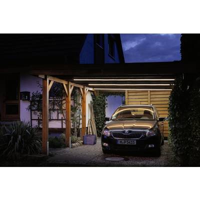 Ein Auto steht abends unter einem beleuchteten Carport neben einem Haus. Die Szene wirkt ruhig und sicher.