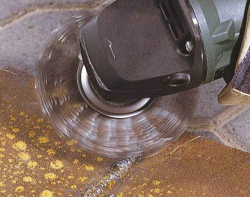 Eine Schleifmaschine, die über eine rostige Metalloberfläche bewegt wird, um Rost zu entfernen. Die Schleifscheibe dreht sich schnell.