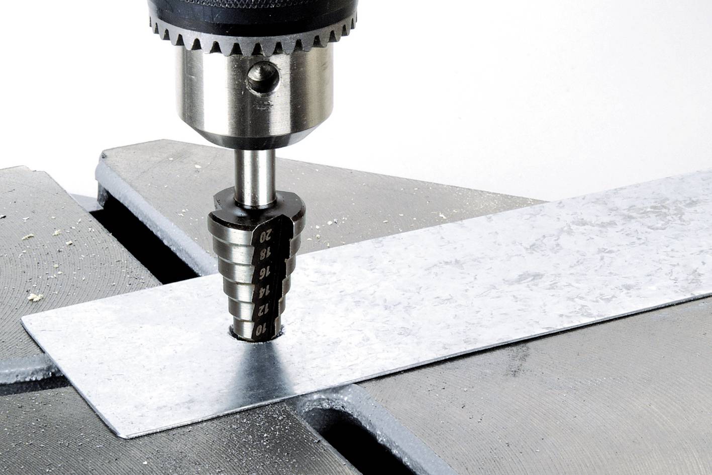Eine Bohrmaschine mit Stufenbohrer bohrt ein Loch in eine Metallplatte auf einem Arbeitstisch.