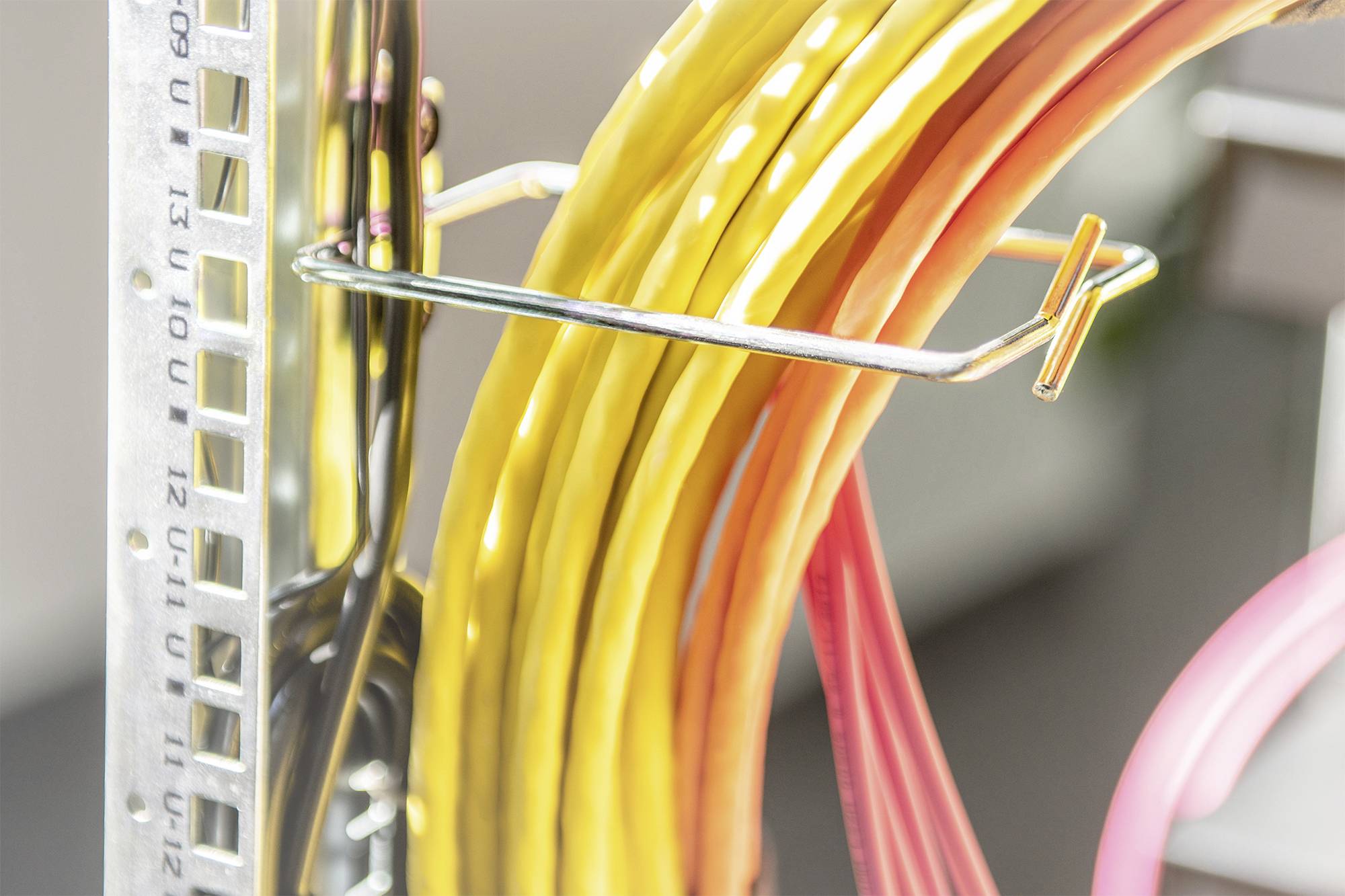'Kabelbündel in Gelb und Rot, auf Metallhaken an einem Netzwerkgestell befestigt.'