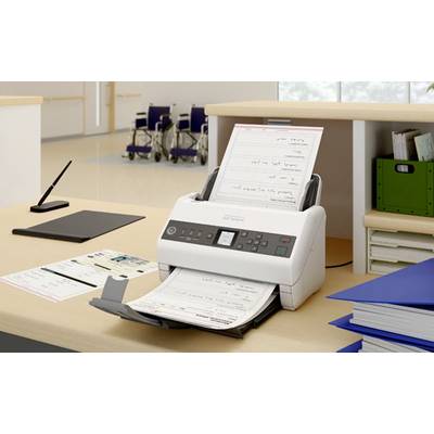 Ein Scanner scannt Dokumente in einem Büro. Auf dem Tisch liegen blaue Ordner und ein schwarzes Klemmbrett. Im Hintergrund stehen Rollstühle.