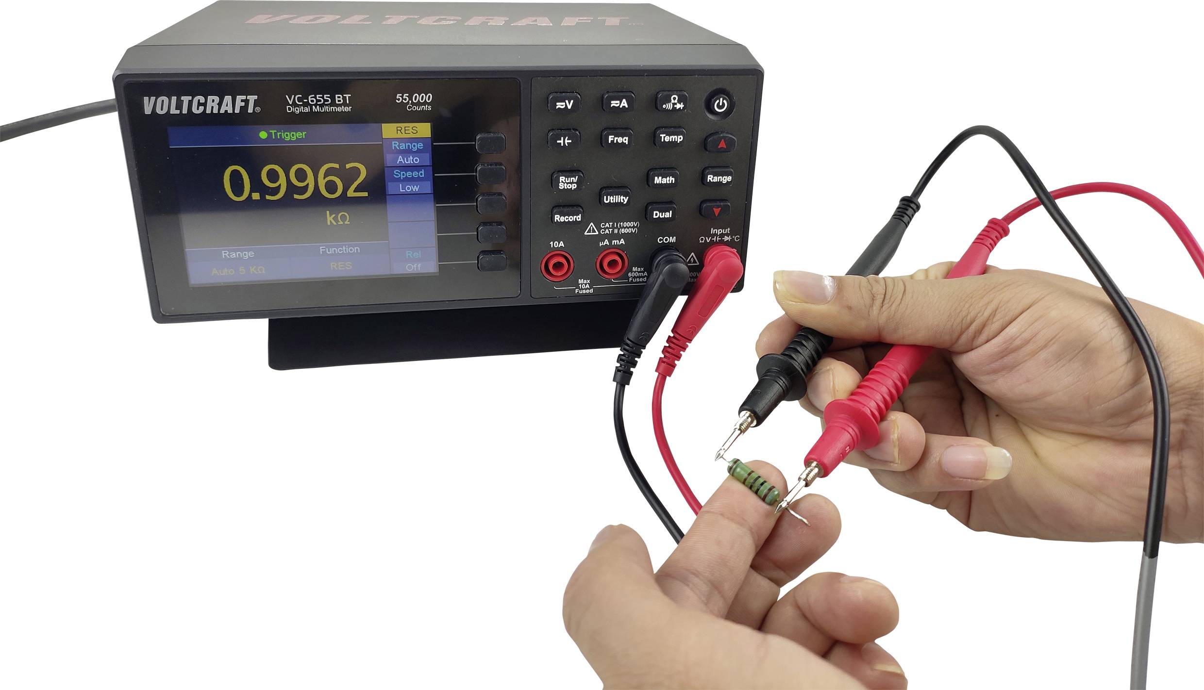 Eine Person misst den Widerstand eines grünen Widerstandsbauteils mit einem digitalen Multimeter, das 0,9962 kΩ anzeigt.