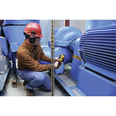 Ein Techniker mit Schutzhelm und Gehörschutz misst mithilfe eines Infrarotthermometers die Temperatur an einem großen blauen Motor.