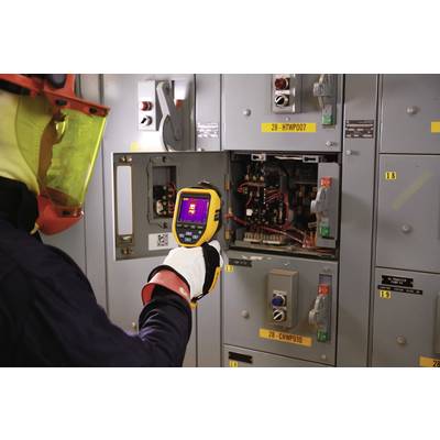 Eine Person mit Schutzkleidung nutzt eine Wärmebildkamera, um die Temperatur von elektrischen Schaltanlagen zu überprüfen.