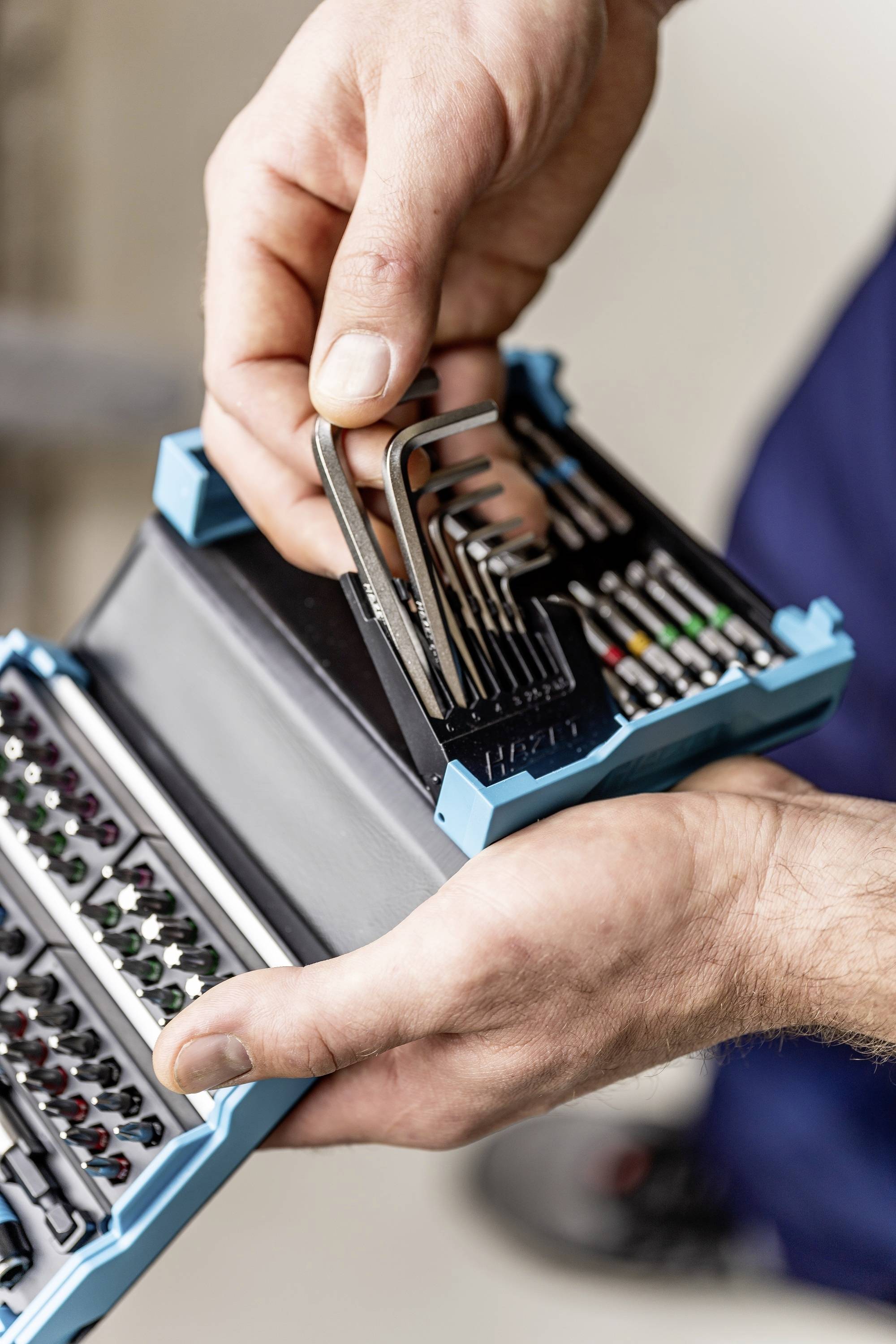 Eine Person hält ein Set von Inbusschlüsseln und Schraubendreheinsätzen in einem blauen Etui. Details und Vielfalt der Werkzeuge erkennbar.