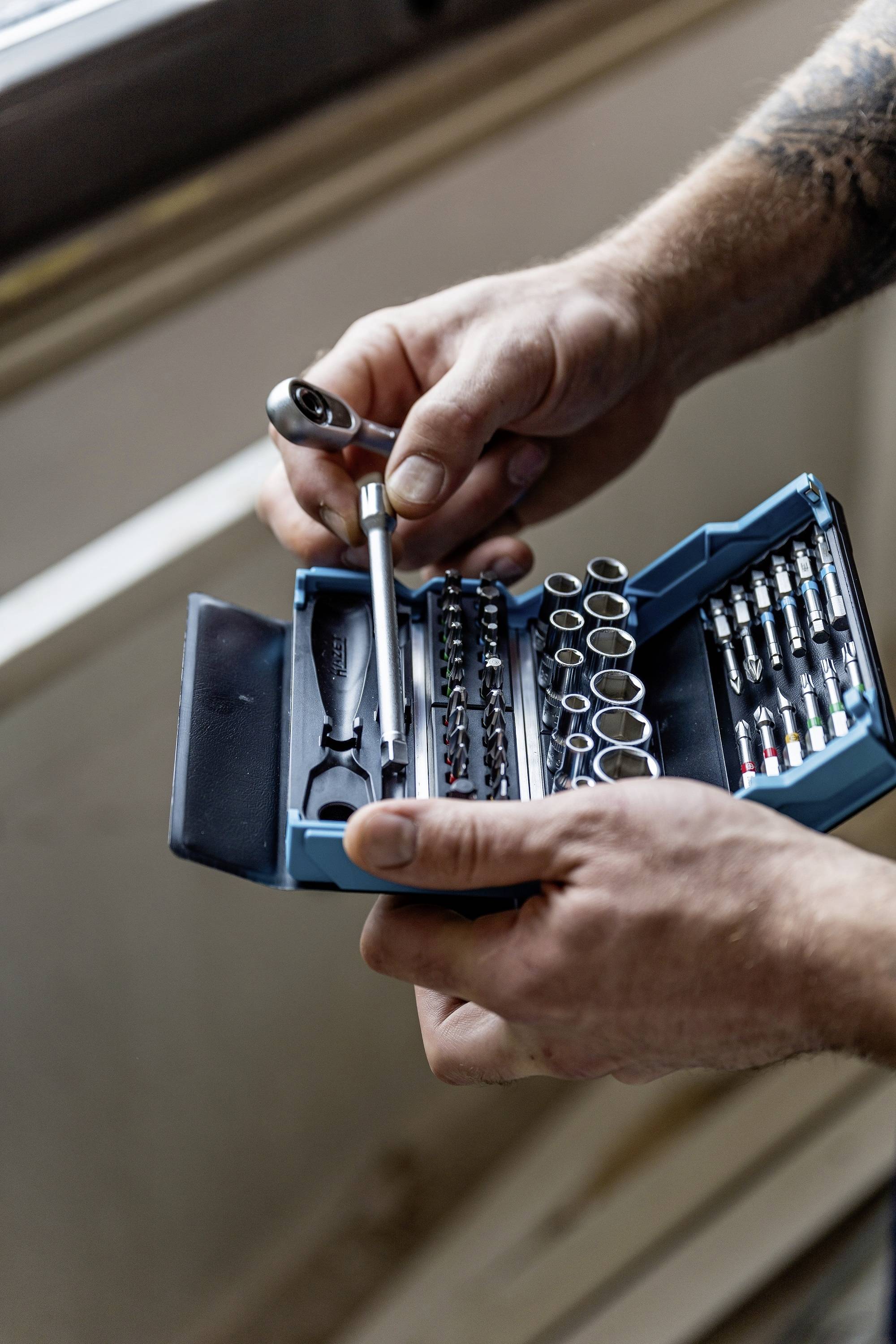 Eine Person hält ein Ratschenkasten mit verschiedenen Aufsätzen, bereit für mechanische Arbeiten.