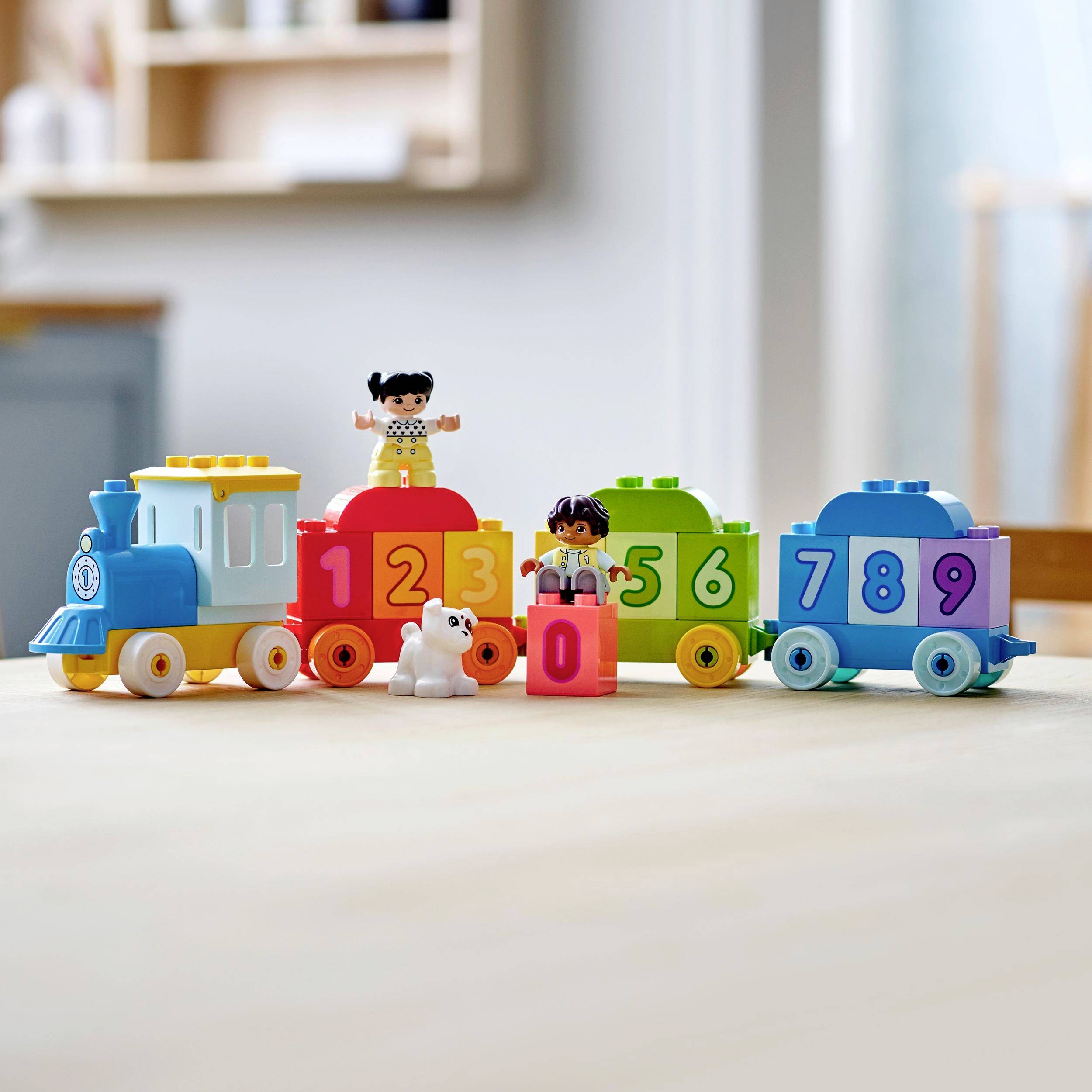 Lokomotive und Waggons mit Zahlen von 0 bis 9 aus bunten Bauklötzen. Zwei Spielfiguren und ein Hund sind dabei.