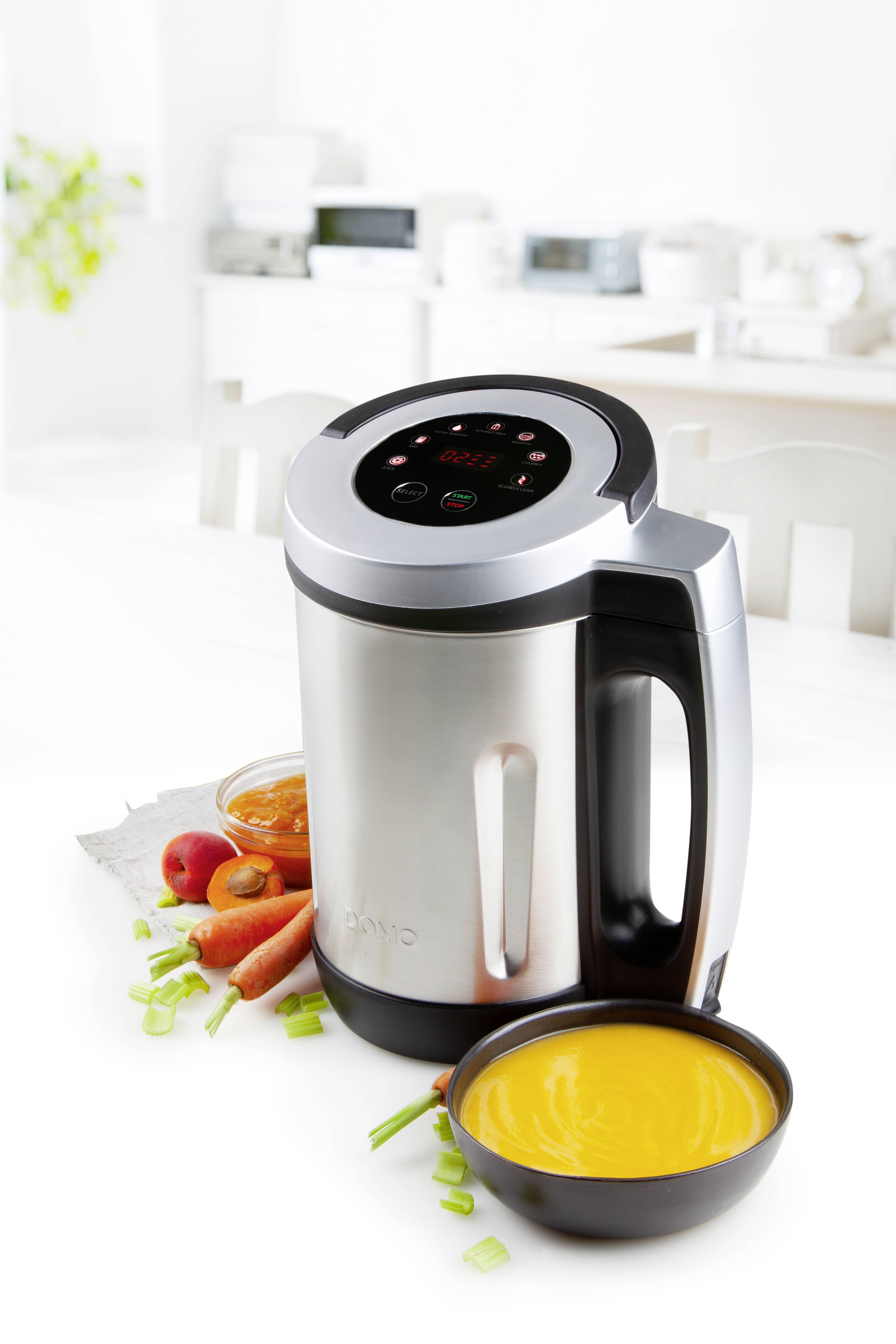 Suppentopf in silberner Küchenmaschine neben Schüssel mit orangefarbener Suppe, Karotten und Zwiebeln, in moderner Küche.