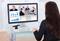 Frau sitzt an einem Tisch und nimmt an einer Videokonferenz teil. Auf dem Bildschirm sind Diagramme und mehrere Konferenzteilnehmer zu sehen.