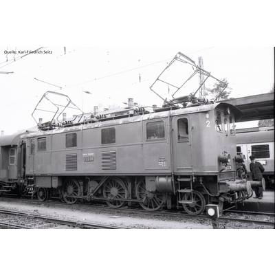 Schwarz-Weiß-Foto einer historischen Elektrolokomotive auf einem Bahnhof. Die Nummer 'E32 28' ist auf der Lokomotive sichtbar. Im Hintergrund steht ein Zug.