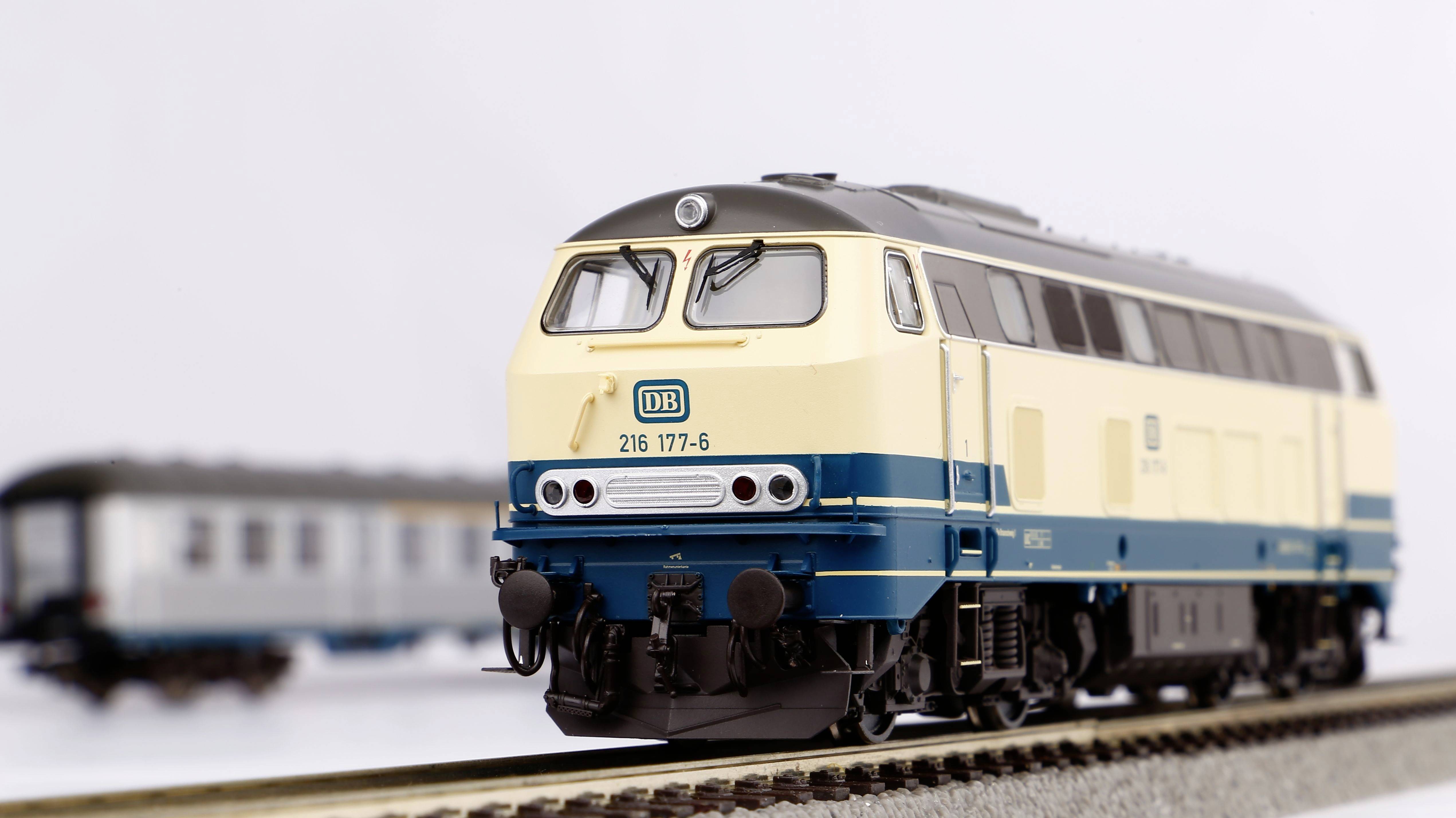 Ein Modell-Lokomotive der Baureihe 216 der Deutschen Bahn in Creme und Blau steht auf einem Gleis; unscharfer Hintergrund zeigt einen Waggon.