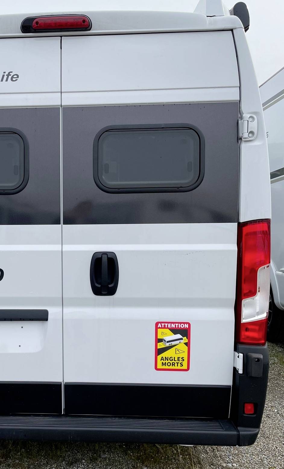 Rückseite eines weißen Transporters mit Warnschild 'Attention angles morts', das auf tote Winkel hinweist.