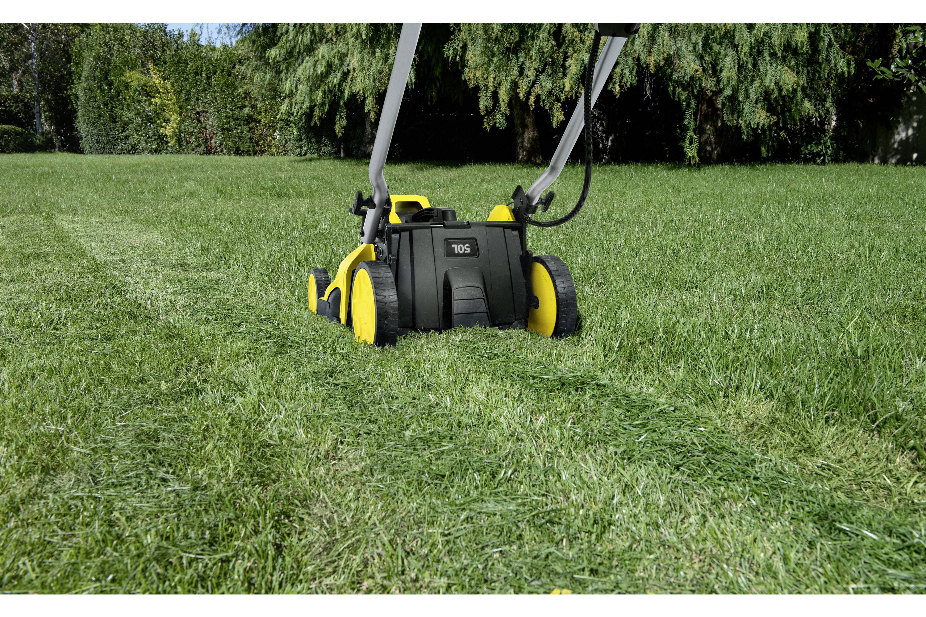 Ein schwarz-gelber Rasenmäher schneidet Gras in einem Garten. Im Hintergrund sind Büsche und Bäume sichtbar.