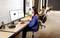 Eine Frau mit Headset arbeitet an einem Computer in einem modernen Büro. Im Hintergrund arbeiten zwei weitere Personen an Schreibtischen.