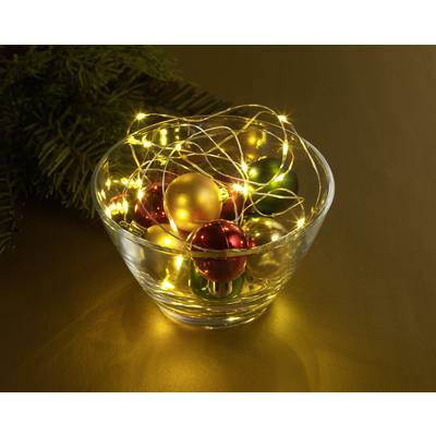 Eine Glasschale voller leuchtender Weihnachtskugeln und Lichterketten auf einem goldenen Hintergrund, daneben Tannenzweige.