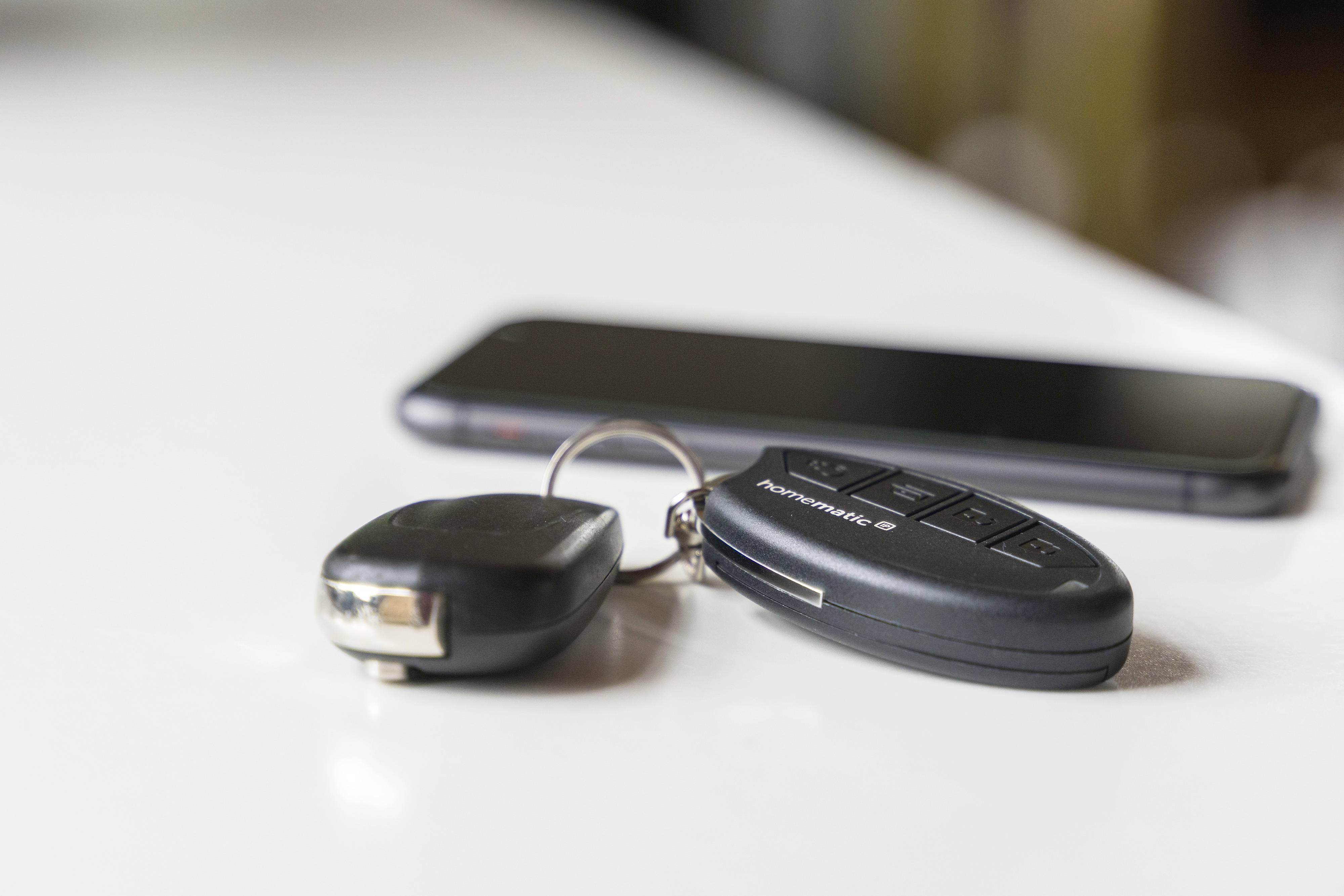 Ein Autoschlüssel und ein Smartphone liegen auf einem Tisch. Der Fokus liegt auf dem Schlüssel, während das Smartphone im Hintergrund unscharf ist.