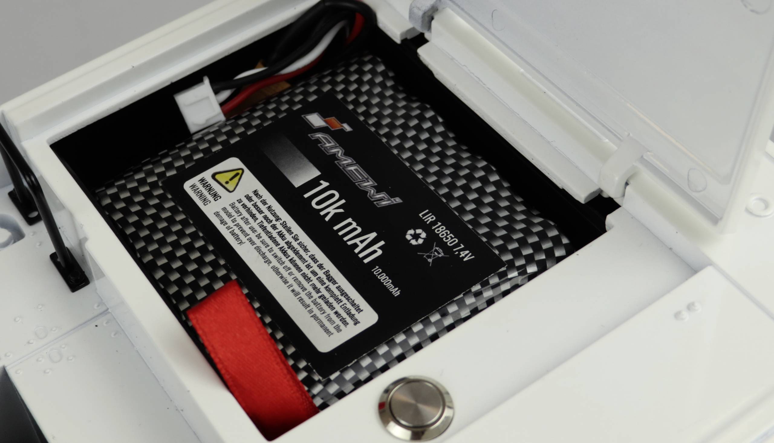 Ein 10.000 mAh Akku liegt in einem offenen Fach. Mehrere Kabel sind angeschlossen. Ein Warnhinweis ist auf dem Akku sichtbar.