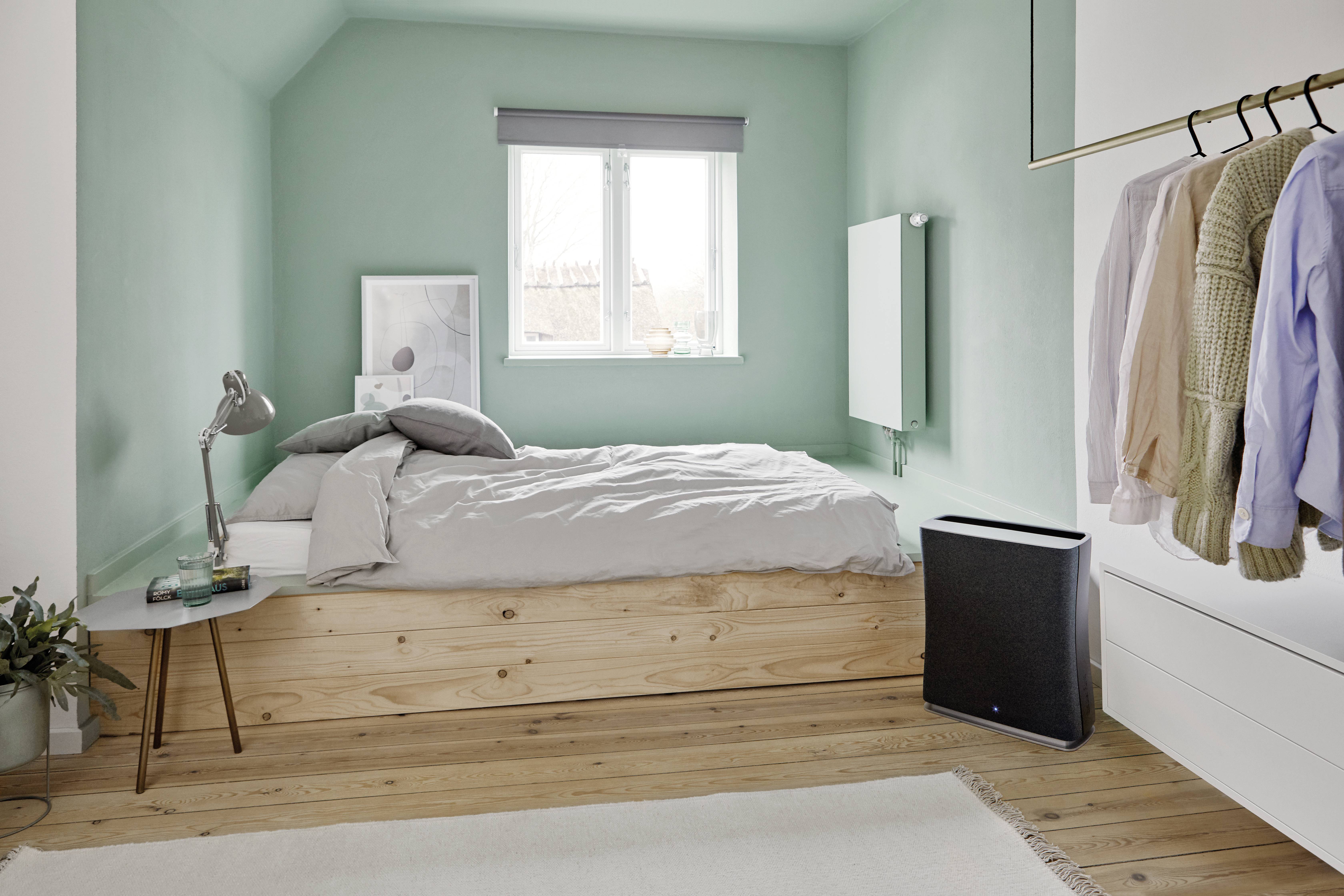 Helles Schlafzimmer mit mintgrünen Wänden, einem Doppelbett aus Holz, Kleiderstange an der Wand und einem Fenster, das Licht hereinlässt.