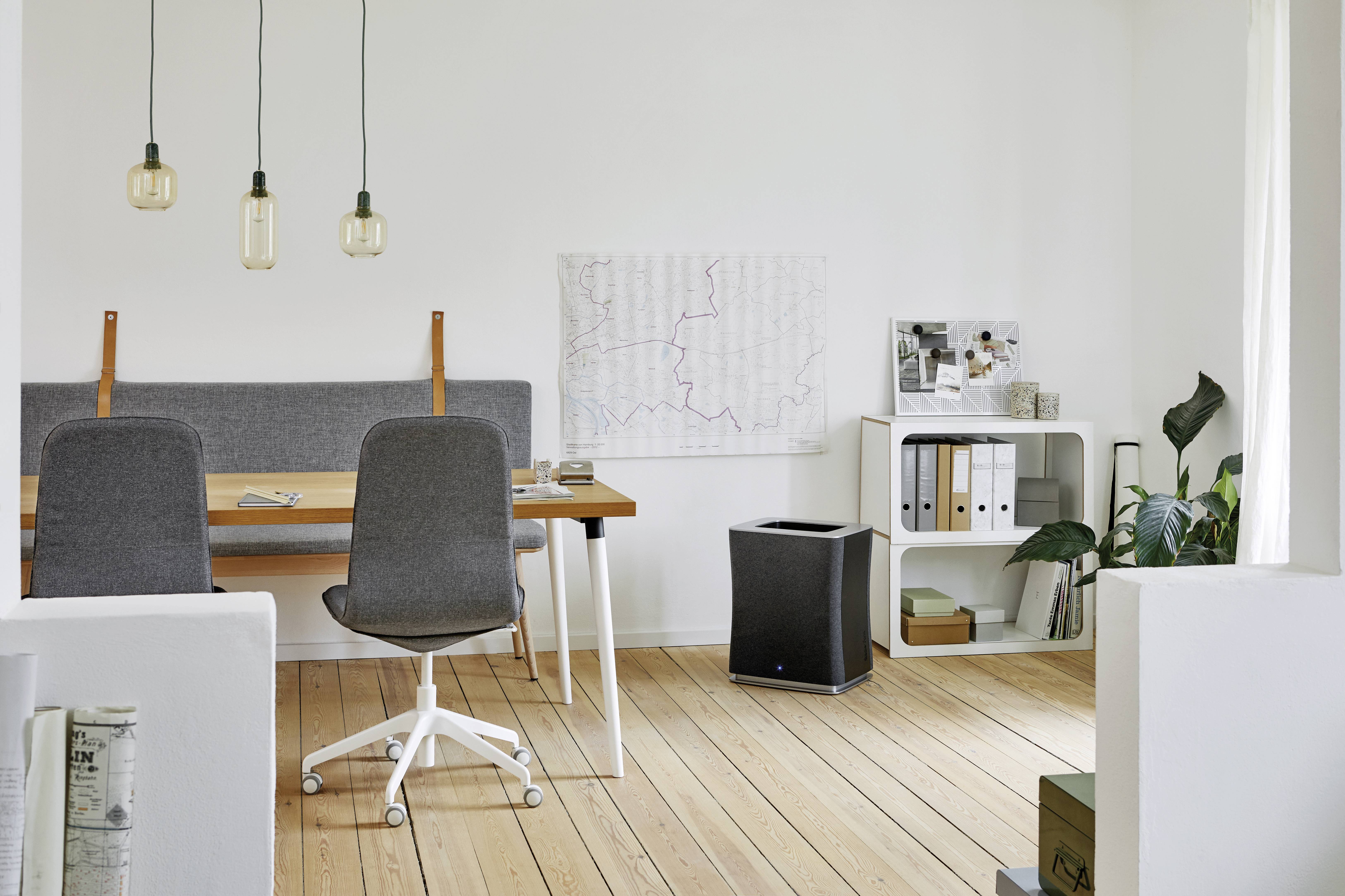 Moderner Büroraum mit Holzboden, zwei grauen Stühlen an einem Tisch, Poster an der Wand, Regal mit Ordnern und Pflanzen im Raum.