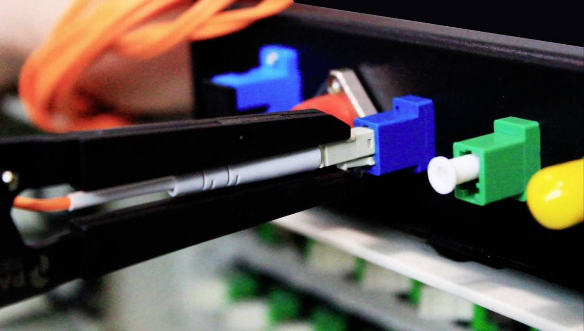 Ein Kabel wird mit einer Zange in einen Netzwerkanschluss gesteckt. Der Anschluss besteht aus farblich unterschiedlich markierten Ports.