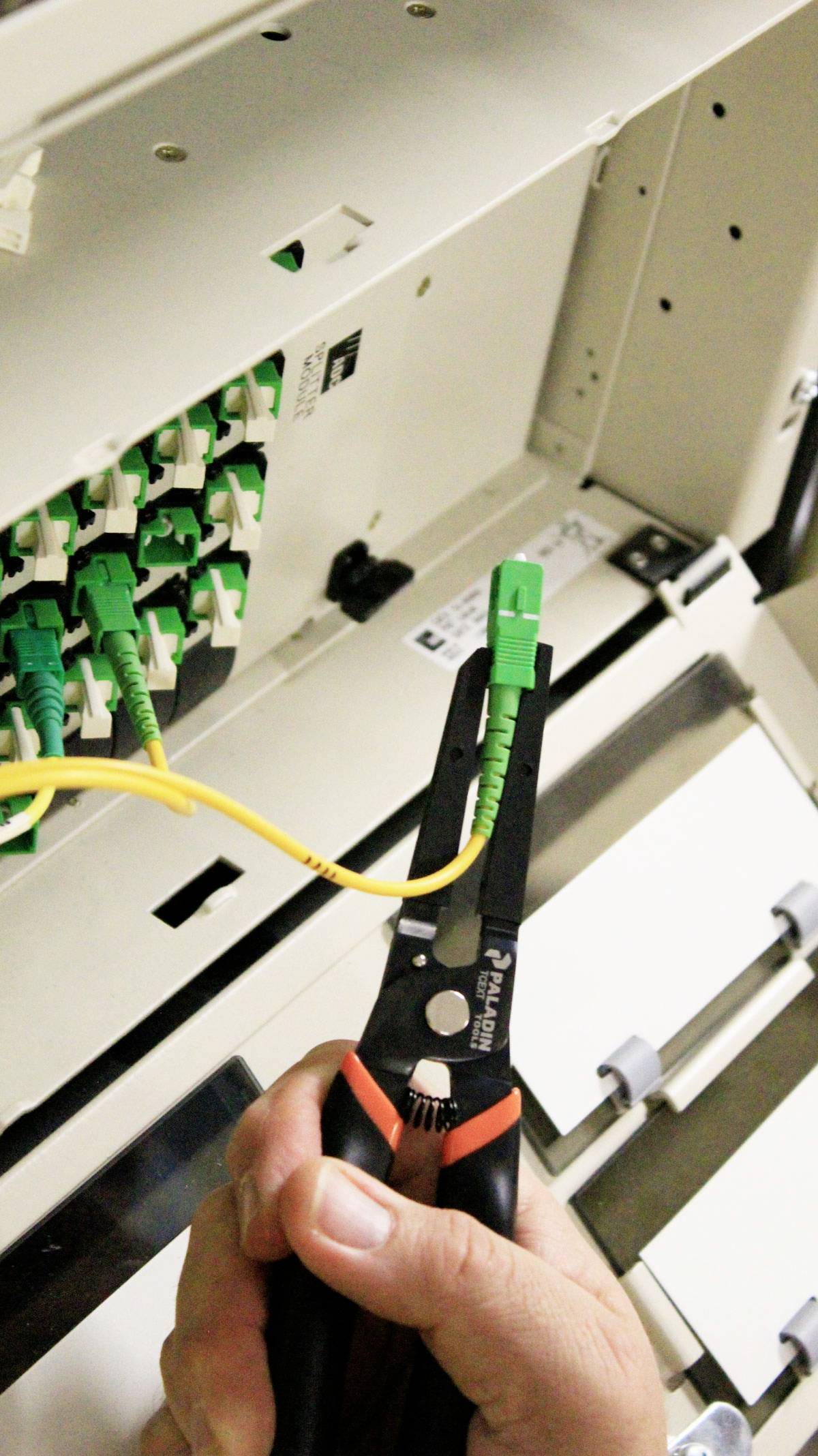 Eine Hand hält eine Zange, die ein gelbes Kabel zu einem grünen Steckverbinder in einem Netzwerkkabelschrank befestigt.