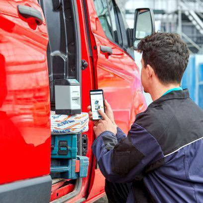 Ein Mann in Arbeitskleidung, der ein Foto von einem geöffneten Lieferwagen mit einem Smartphone macht. Werkzeug und Pakete sind sichtbar.