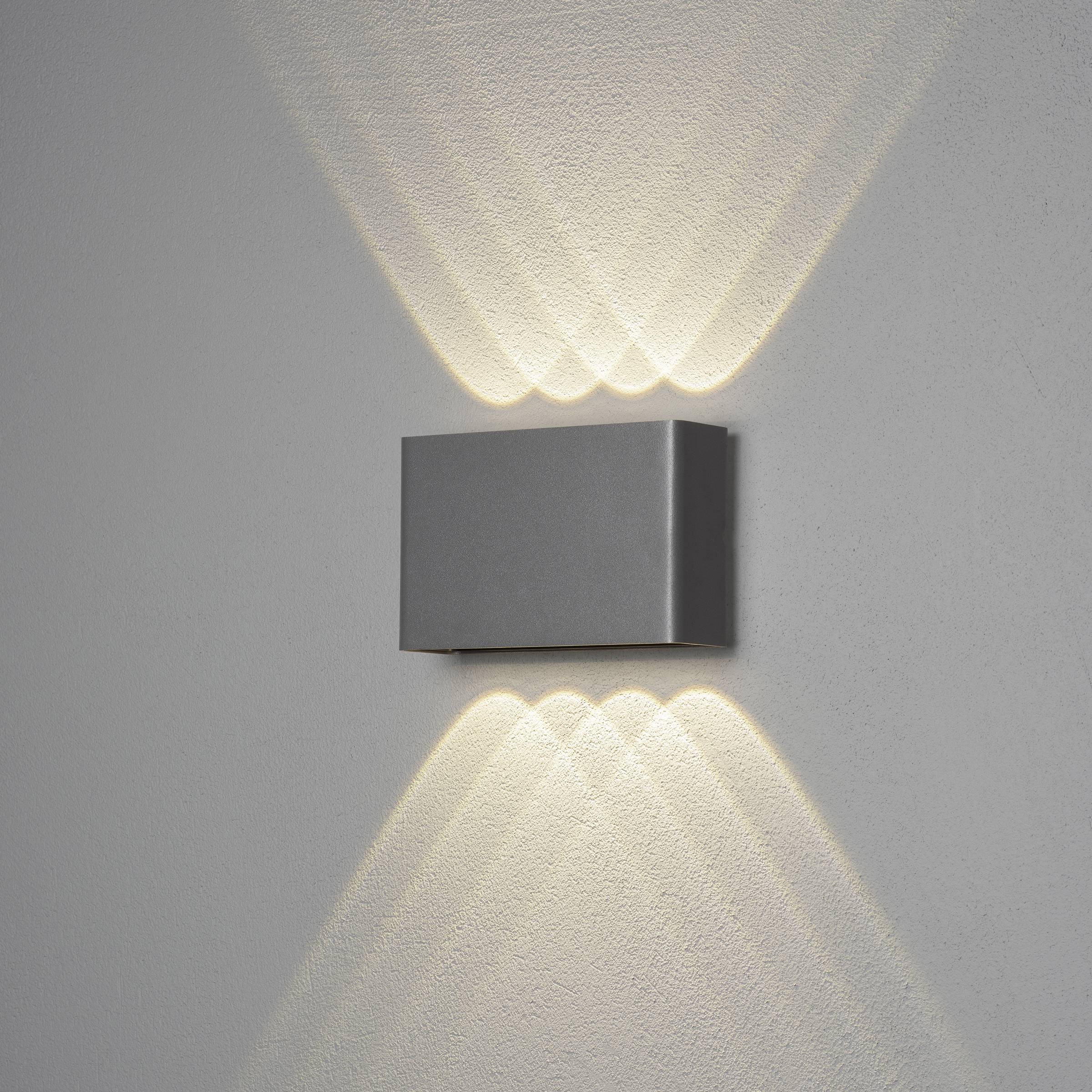 Moderne Wandleuchte mit rechteckigem Gehäuse, die warmes Licht nach oben und unten abstrahlt, erzeugt ein dekoratives Muster an der Wand.