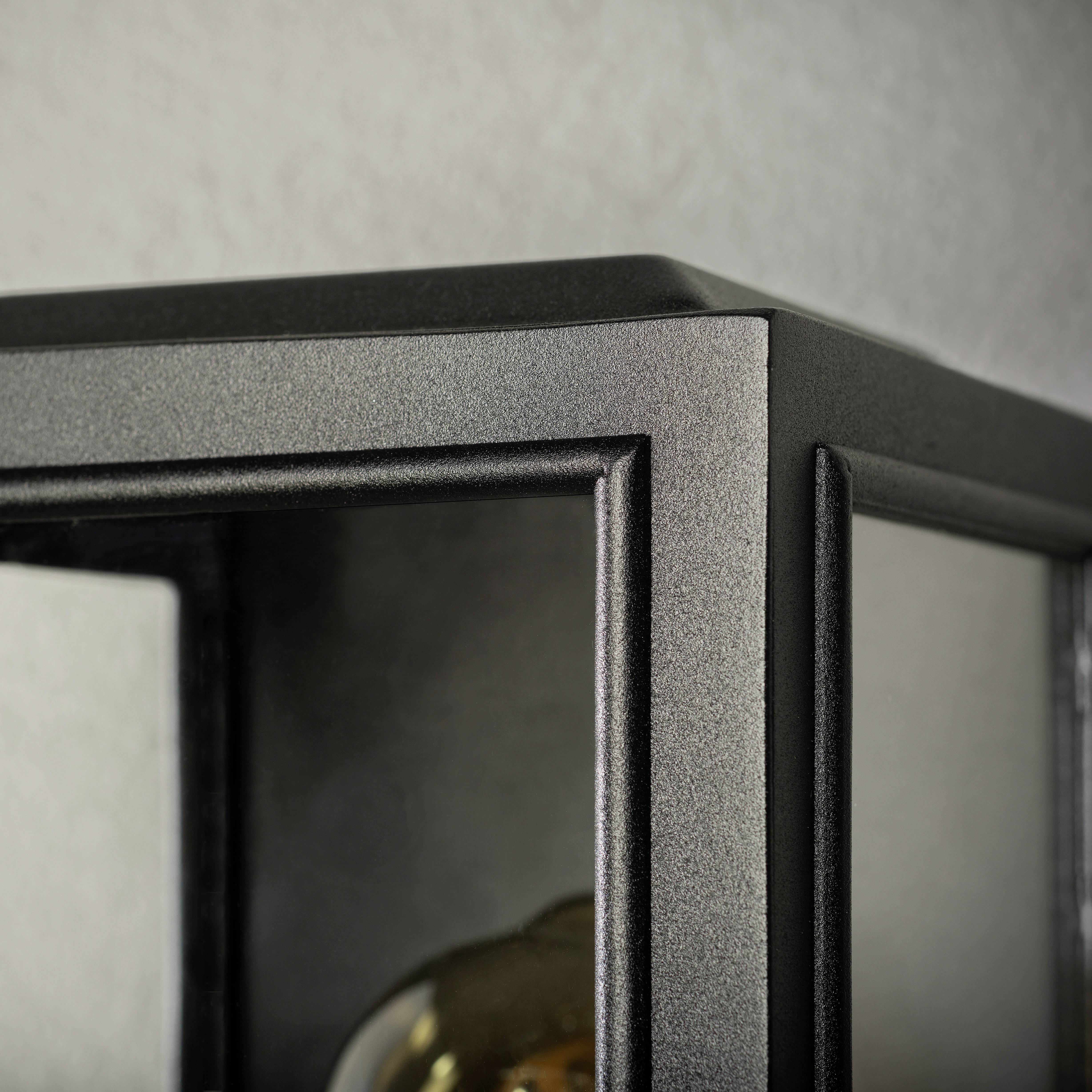 Metallische Ecke eines Lampenschirms mit klarem Glas und einer Glühbirne im Inneren, teilweise sichtbar im Hintergrund.